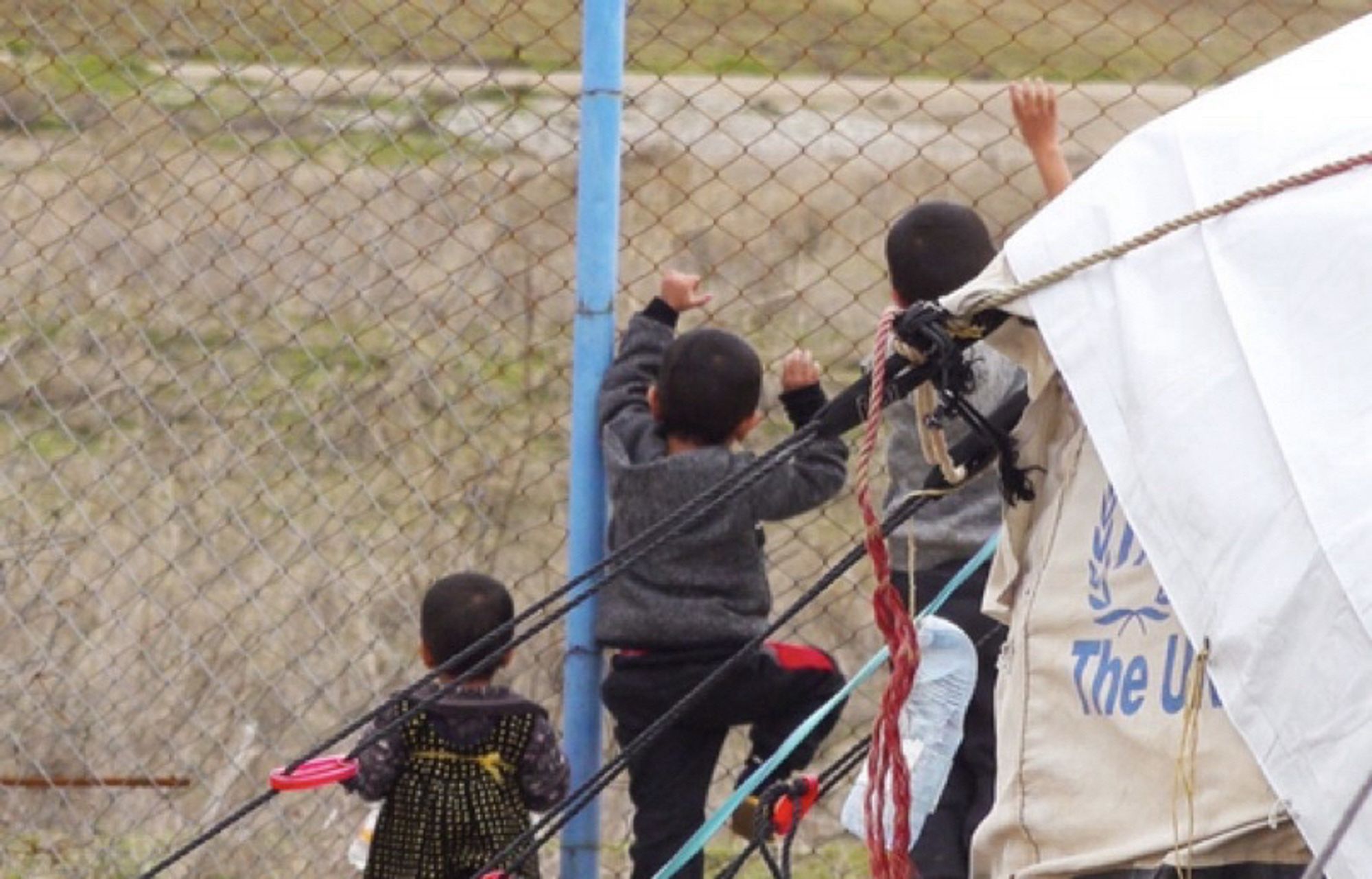 Des enfants derrière les grilles d’un camp.