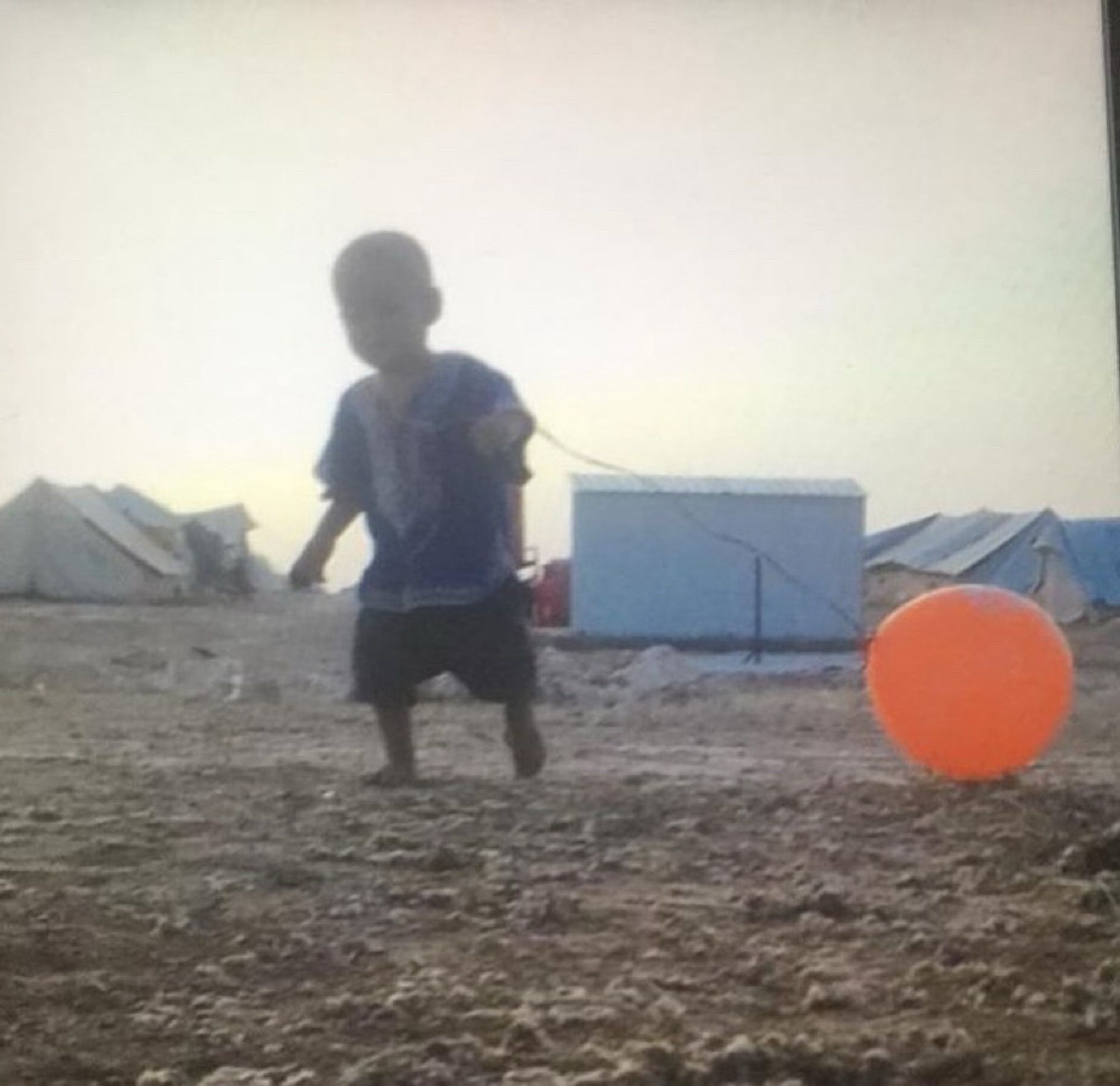 Un enfant avec un ballon orange dans un camp.