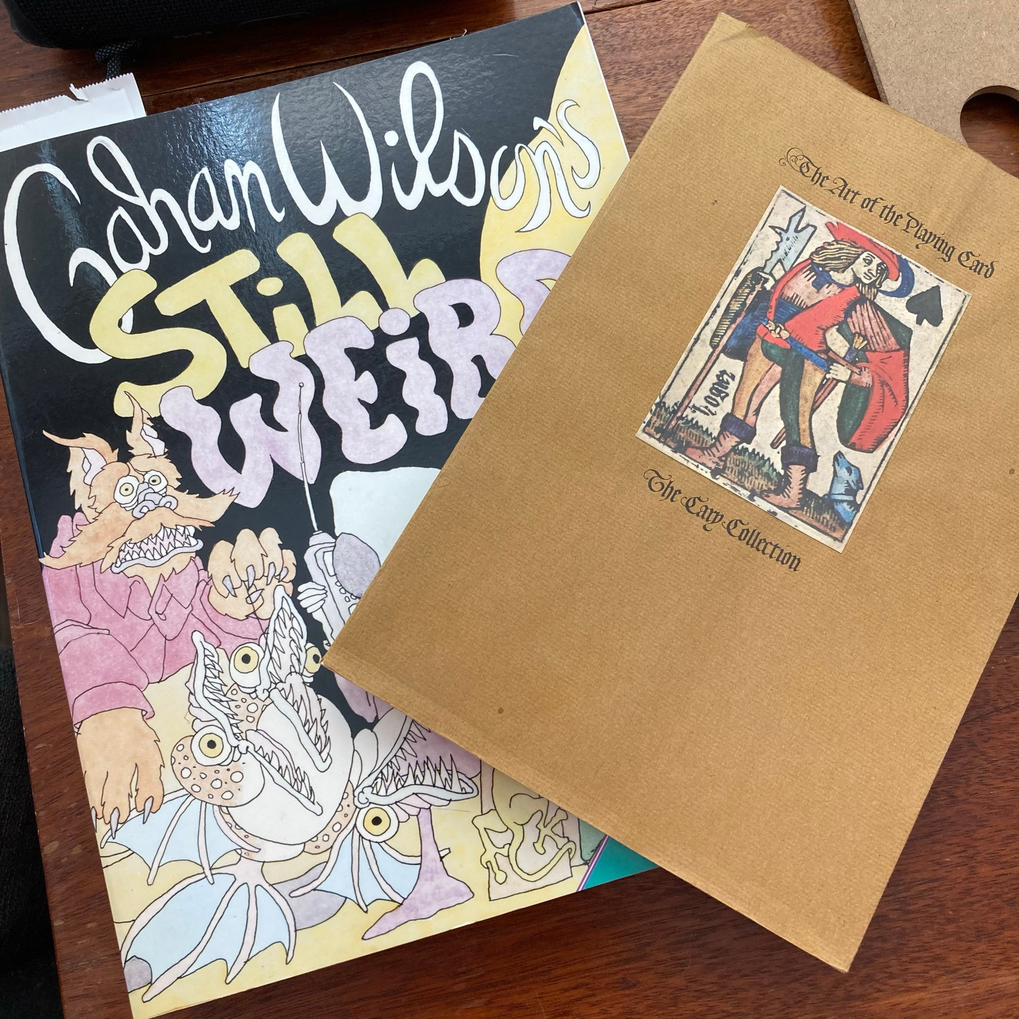 A copy of Gahan Wilson’s “Still Weird” and a book or museum catalog called “The Art of the Playing Card.”