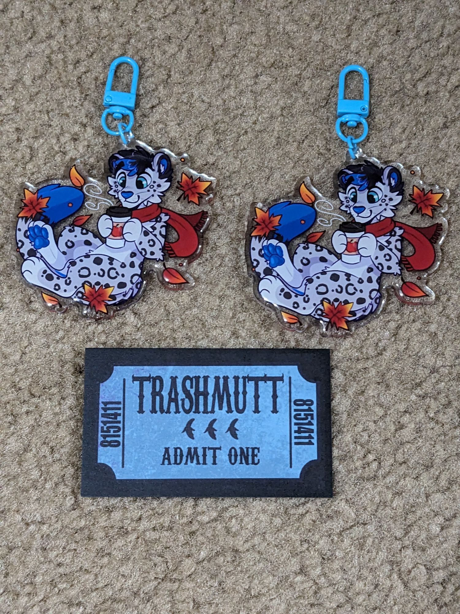 Two keychains featuring Sebastian the snow leopard and a card reading TRASHMUTT ADMIT ONE