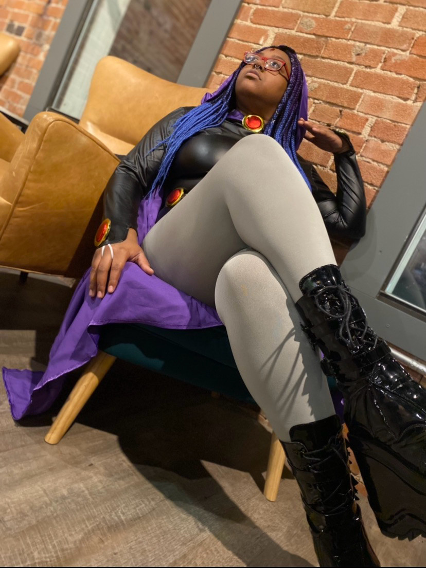 Raven cosplayer sitting crisscrossed looking into the distance 
