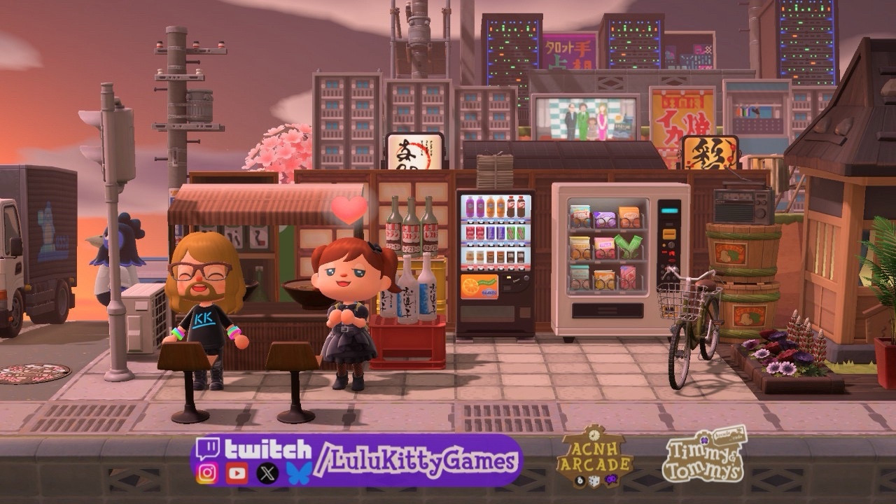 A scene from the game Animal Crossing: new horizons - a character on the left has long wavy blond hair, a beard, and glasses and is wearing a DJ KK shirt. The character on the left is wearing the visual-punk dress and has auburn hair in pigtails. They are in front of a stall with ramen bowls, bottle crates, and decorative bottles. The scene is a cityscape with a street and truck item on the left and skyscrapers in the background made of simple panels and servers. To the right is Walt’s house and a cruiser bike.