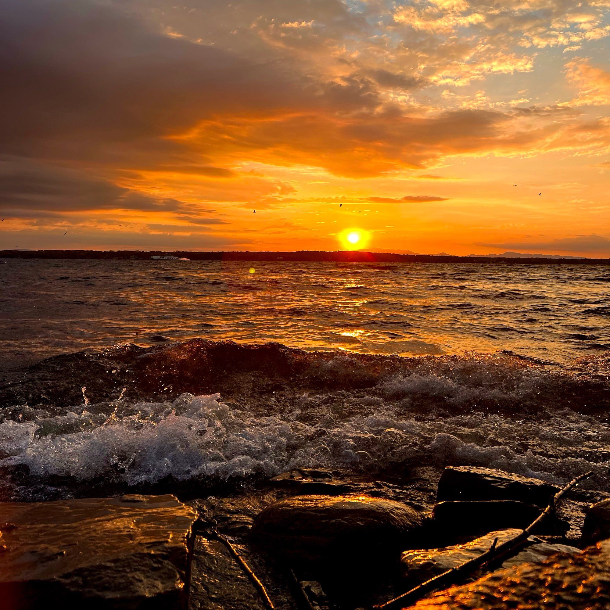 Sun rising over the horizon reflecting sunlight on a large lake with waves in the foreground