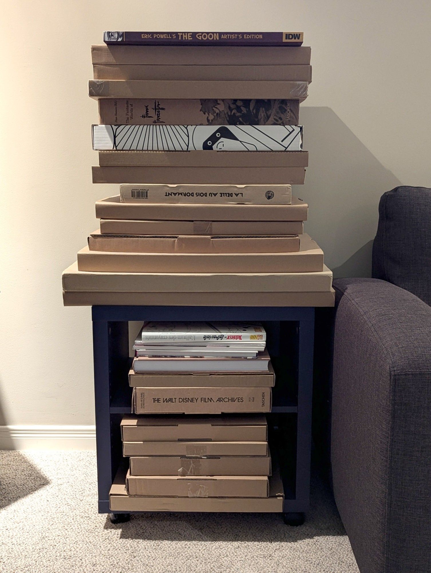 A tall pile of artist's editions and other similarly sized artbooks stacked vertically in and on an old piece of Ikea furniture that resembles an oversized 1x1 Kallax cube.