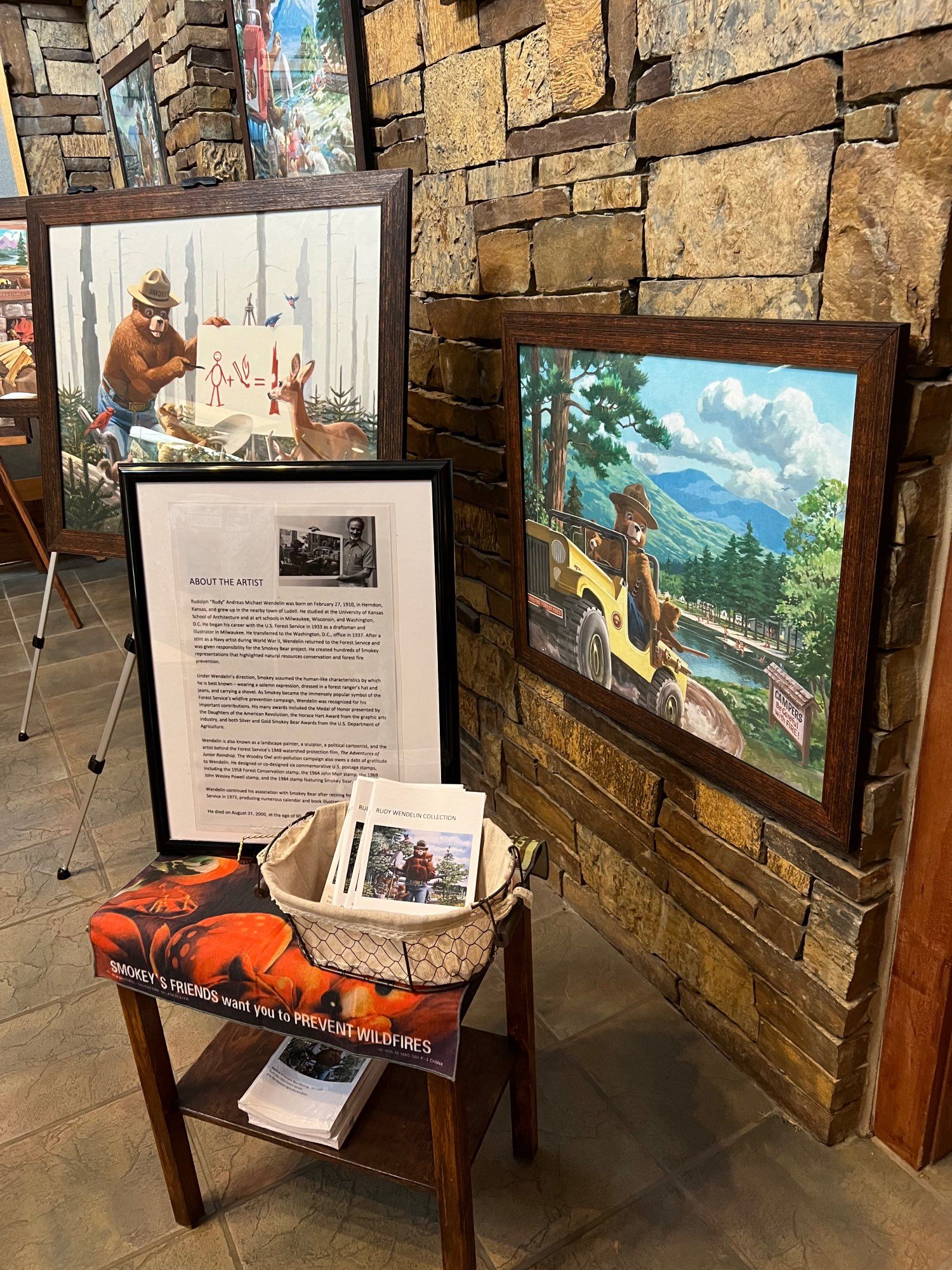 Paintings of Smokey Bear and a basket of brochures about artist Rudy Wendelin