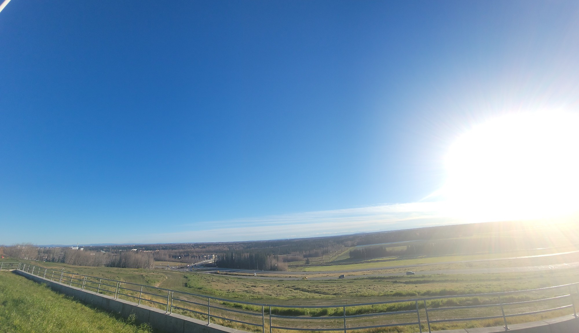 A panorama view from the hill at UAFs Troth Yeddha campus. The sun is glaringly bright in a cloudless sky over a brownish green terrain