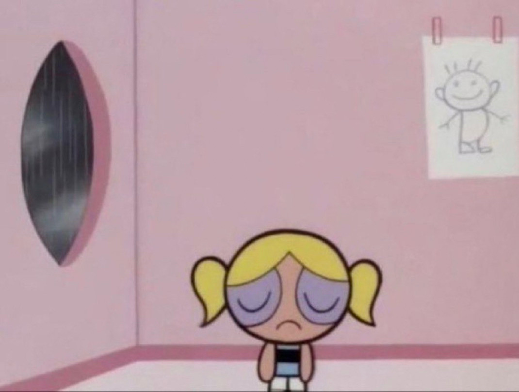 Bubbles from the show The Powerpuff Girls. She’s standing in a pink bedroom while it rains outside, looking sad with her head hanging and her eyes closed. She has blonde pig tails and is wearing a blue dress.