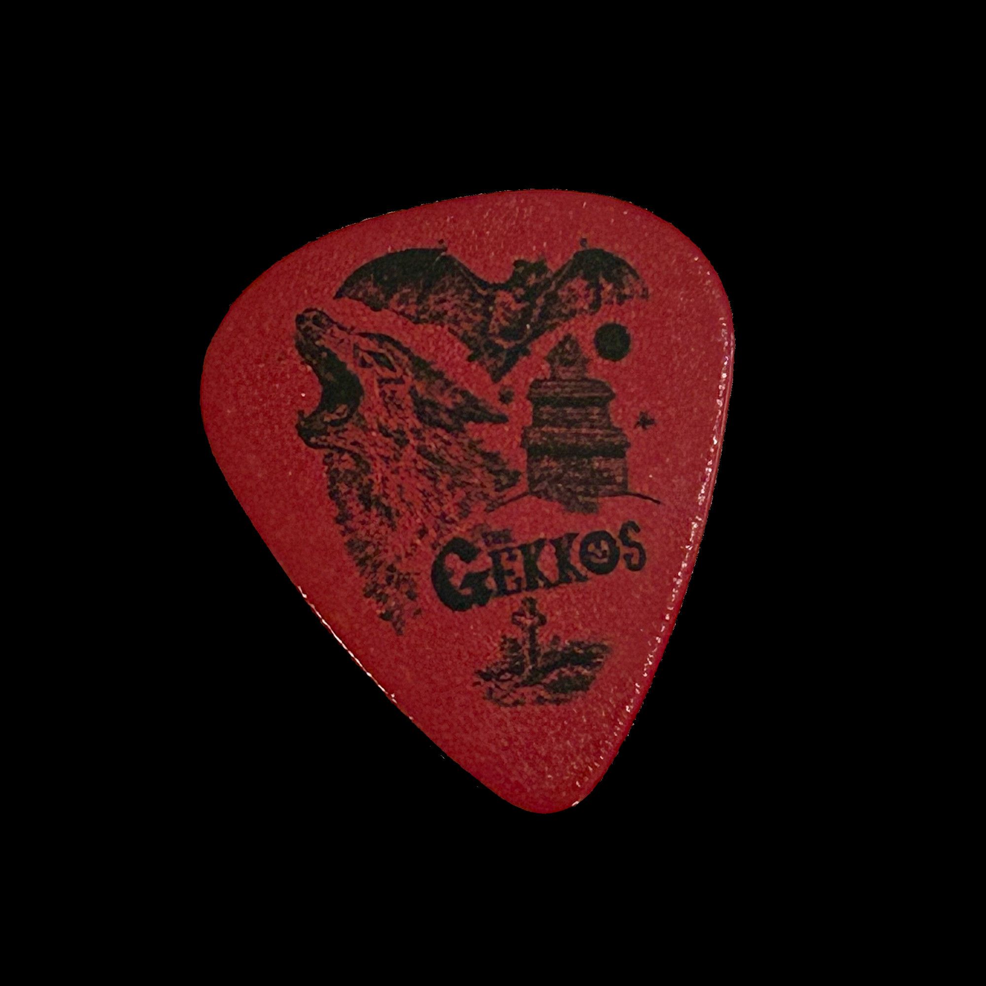 Red guitar pick featuring black line art of a howling wolf, vampire bat, gravestone, and haunted house. It says The Gekkos.