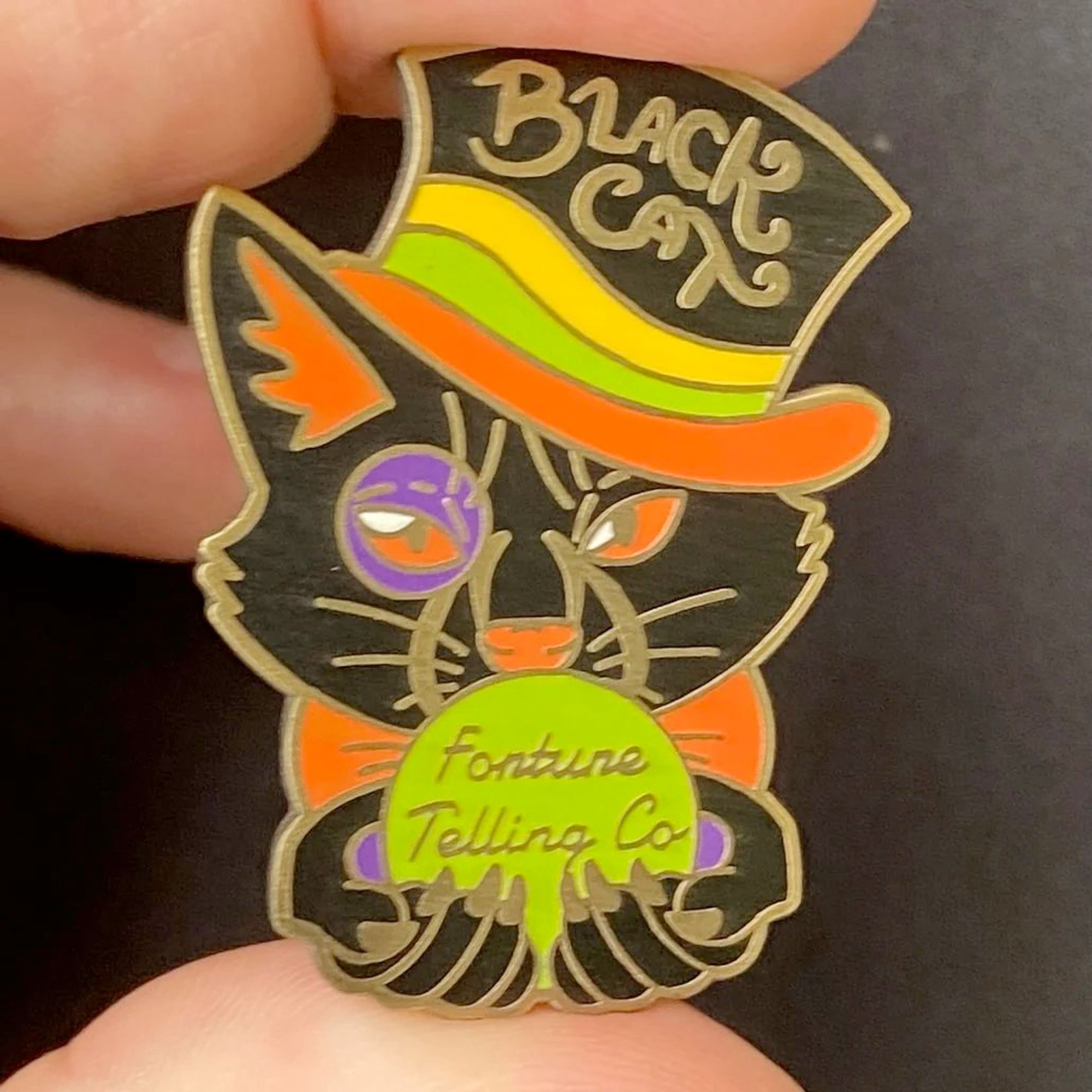 Enamel pin of a black cat wearing a top hat and holding a crystal ball. It says "Black Cat Fortune Telling Co"