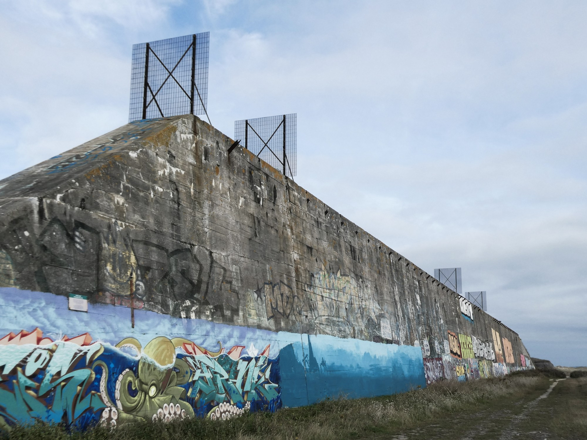 Another angle on the wall showing detail of richly coloured graffiti depicting an octopus under the waves. Metal fences top the wall.