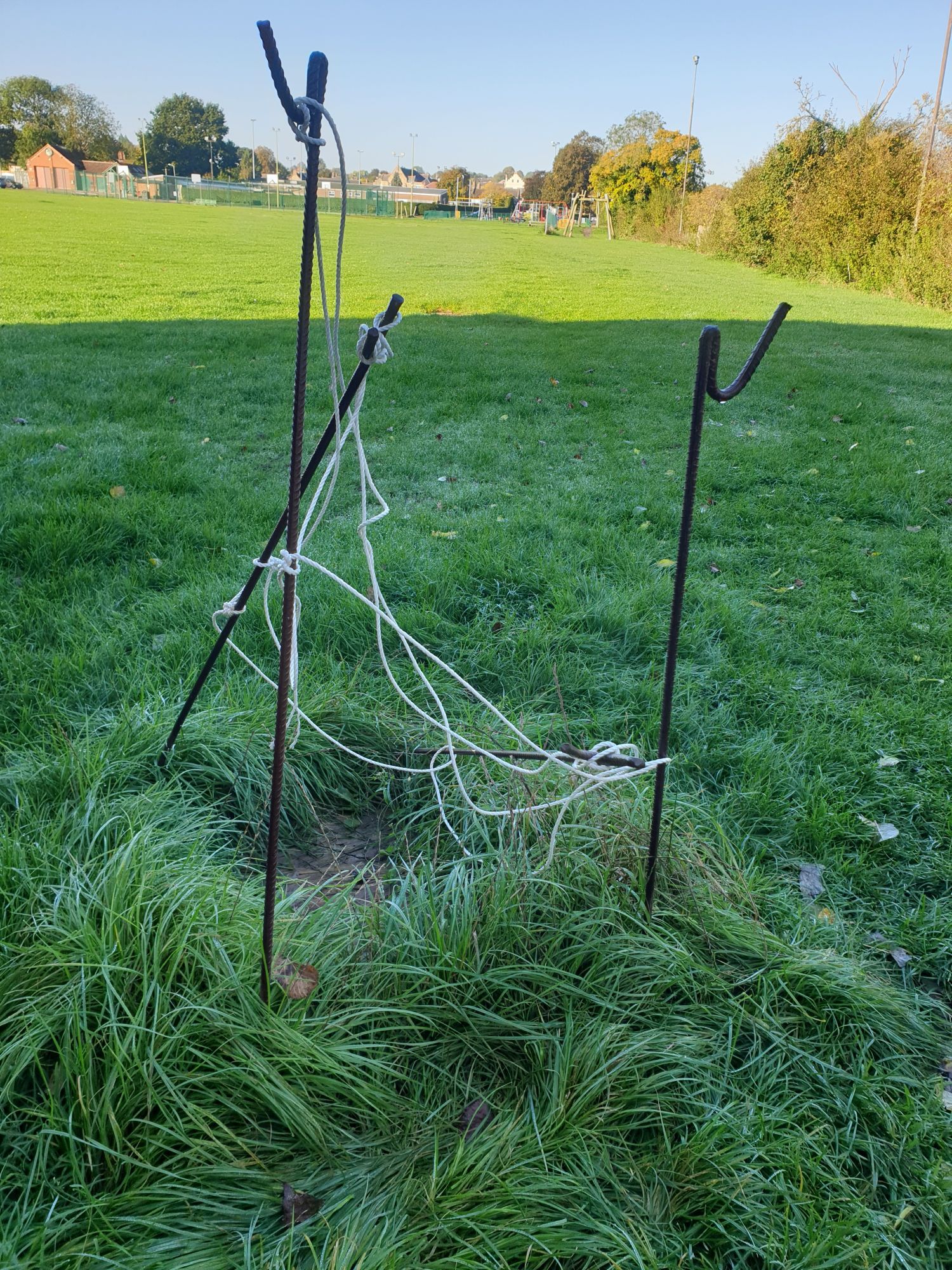 Three metal posts standing at angles to each other at the edge of a playing field, with narrow white rope looped around them.