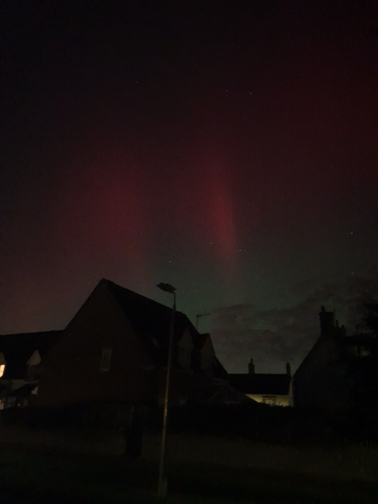 Dark rooftops, and above them in the night sky, plumes of crimson and green aurora borealis.