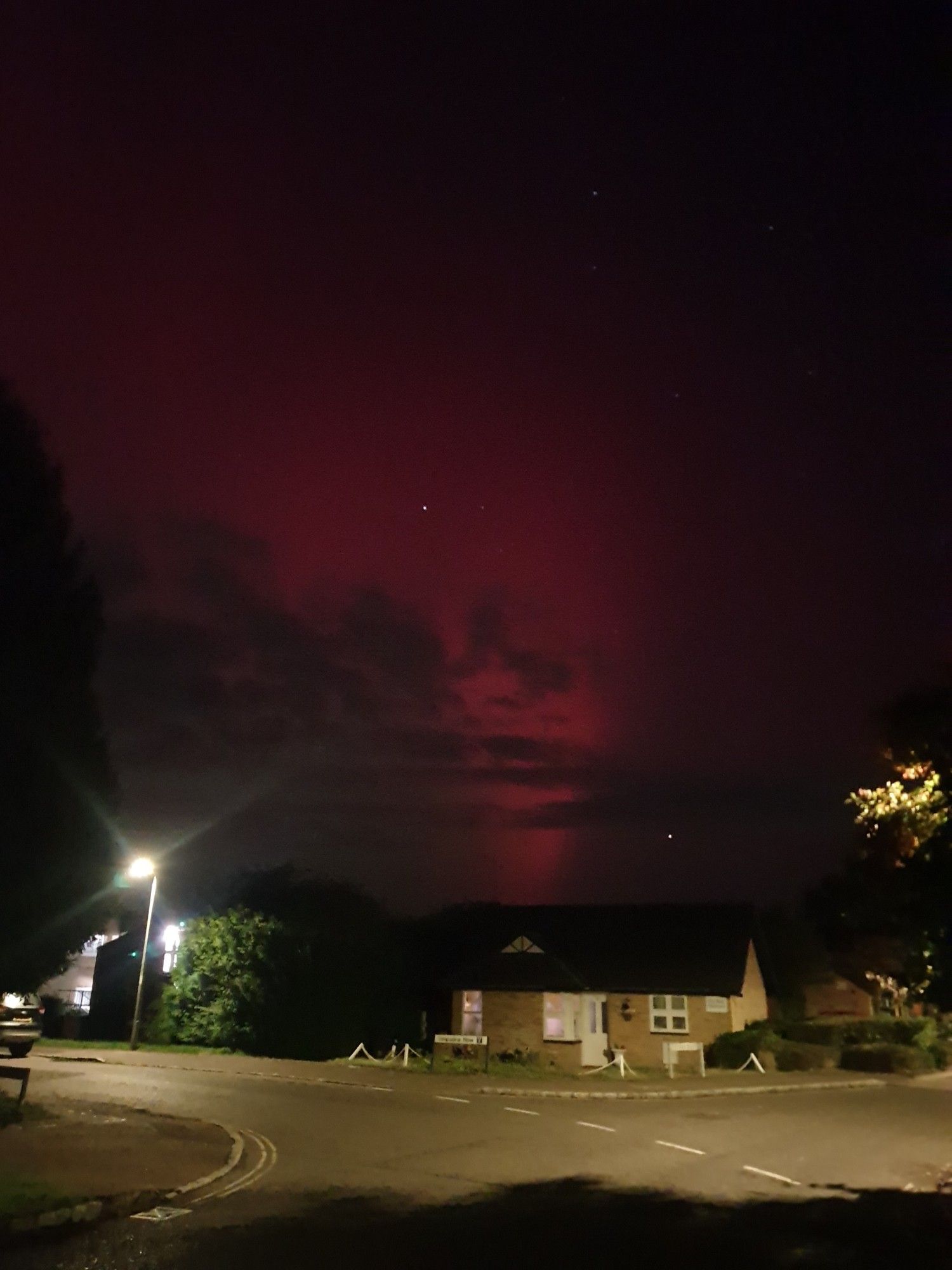 Night time. A very ordinary bungalow by lamplight and above it a huge slew of crimson aurora borealis across the night sky.