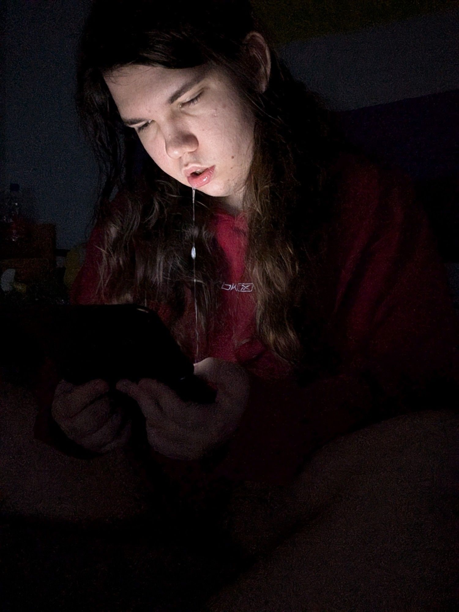 A long-haired person staring at a Nintendo 3DS, drooling and with heavy eyes.