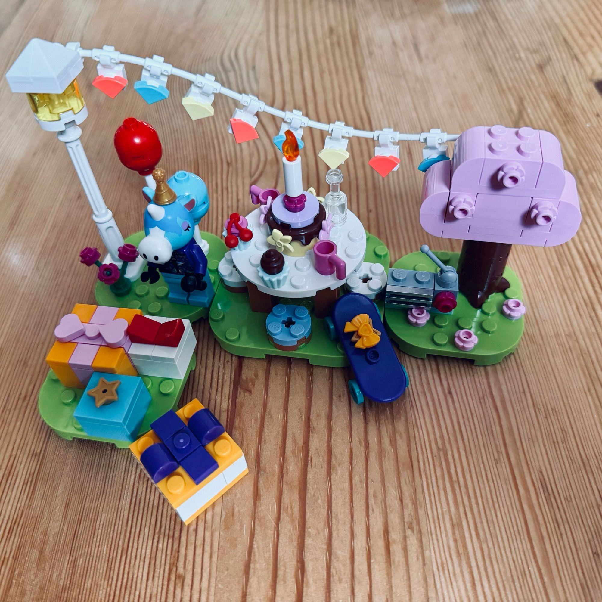 Eine farbenfrohe Lego-Szene mit einer Geburtstagsfeier mit einem Kuchen, Geschenken und dekorativen Elementen wie einer Lampe und Luftballons. Die Einrichtung umfasst einen Baum und verspielte Charaktere, die eine festliche Atmosphäre schaffen.