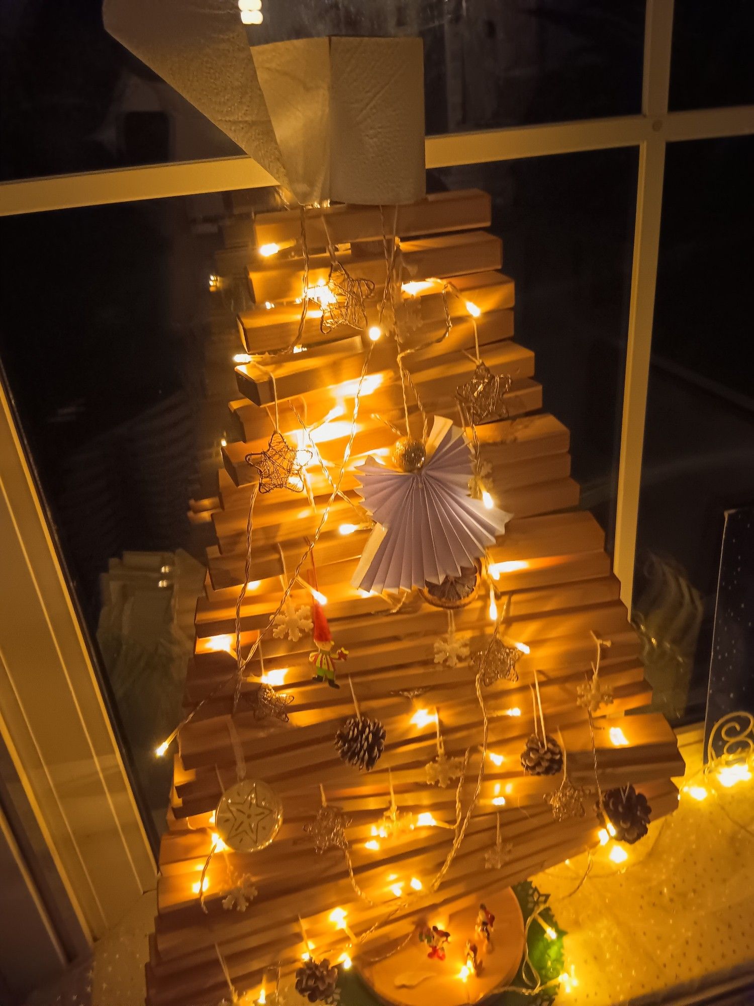 Ein beleuchteter und geschmückter Tannenbaum aus Holz - die Spitze schmückt eine abgerollte Klopapierrolle