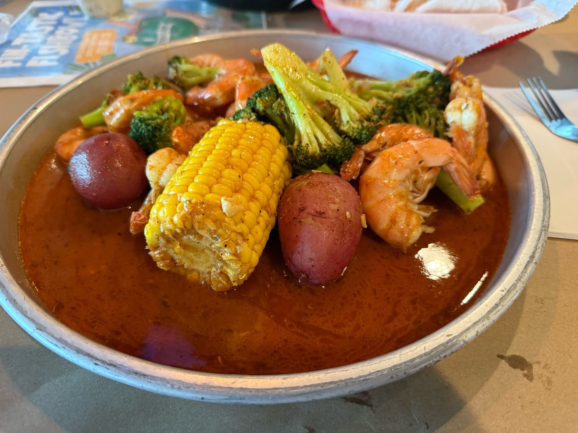 Shrimp boil plate featuring corn, potatoes, and broccoli all in seasoned garlic butter.