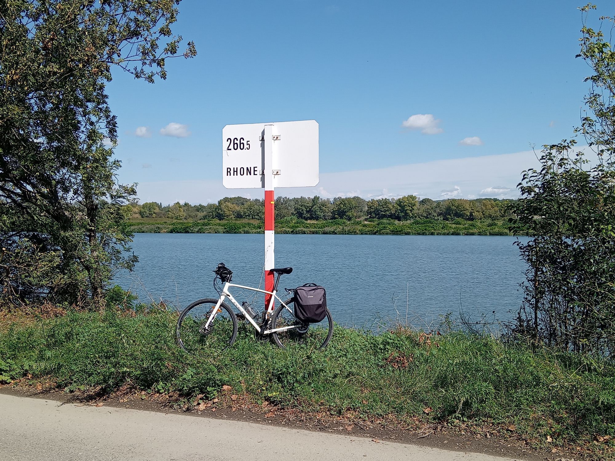 Bicycle propped against kilometre marker sign by River Rhône. Blue sky.