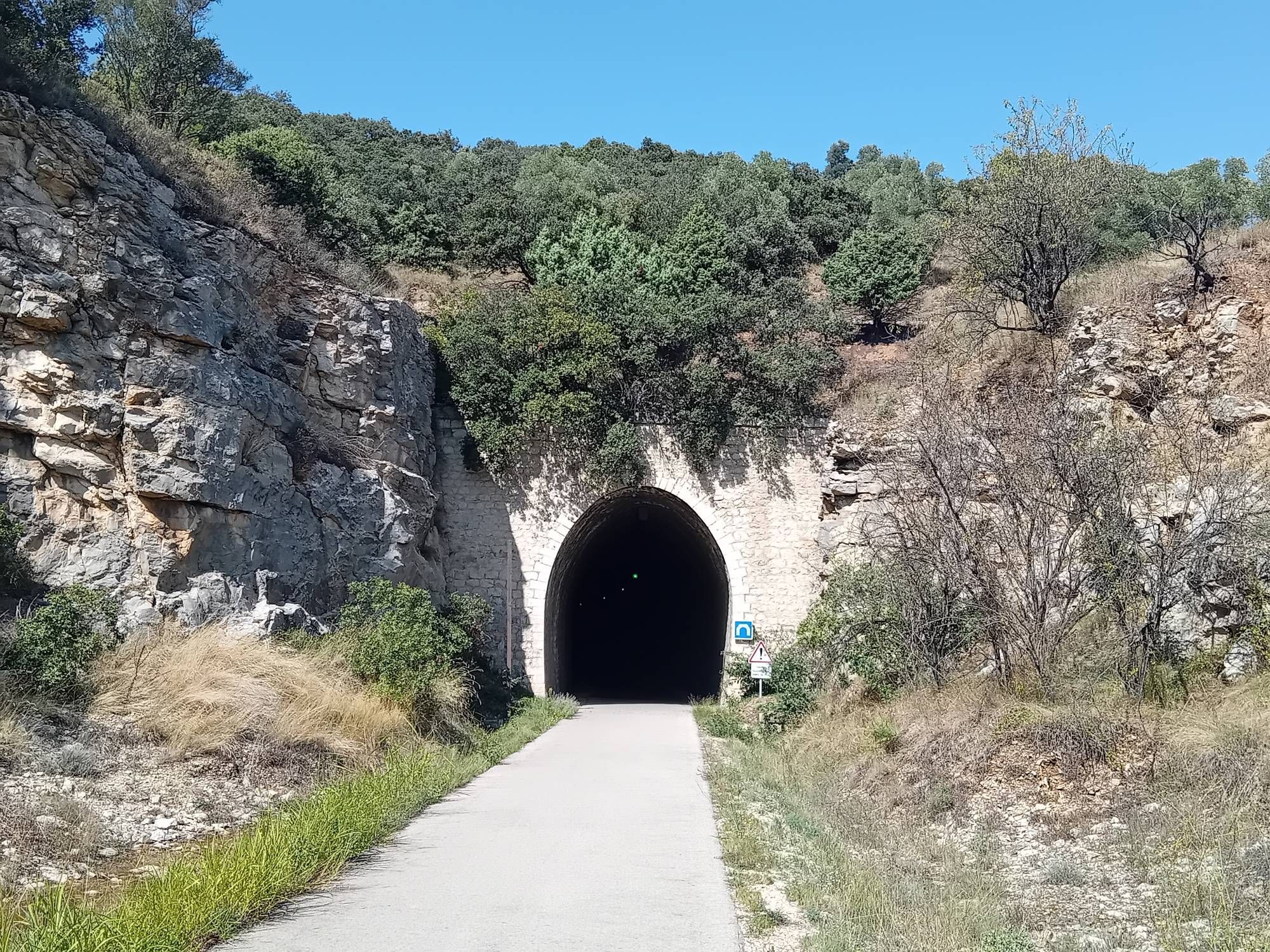 Tunnel entrance on cycle track with greenery and blue sky above. The tunnel is an old railway tunnel, now lit for cyclists.