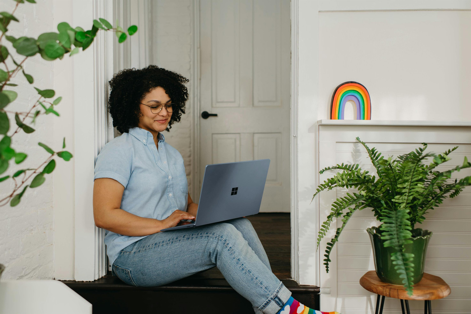 A photo of a woman on her laptop. A rainbow sticker is on the wall near her. 