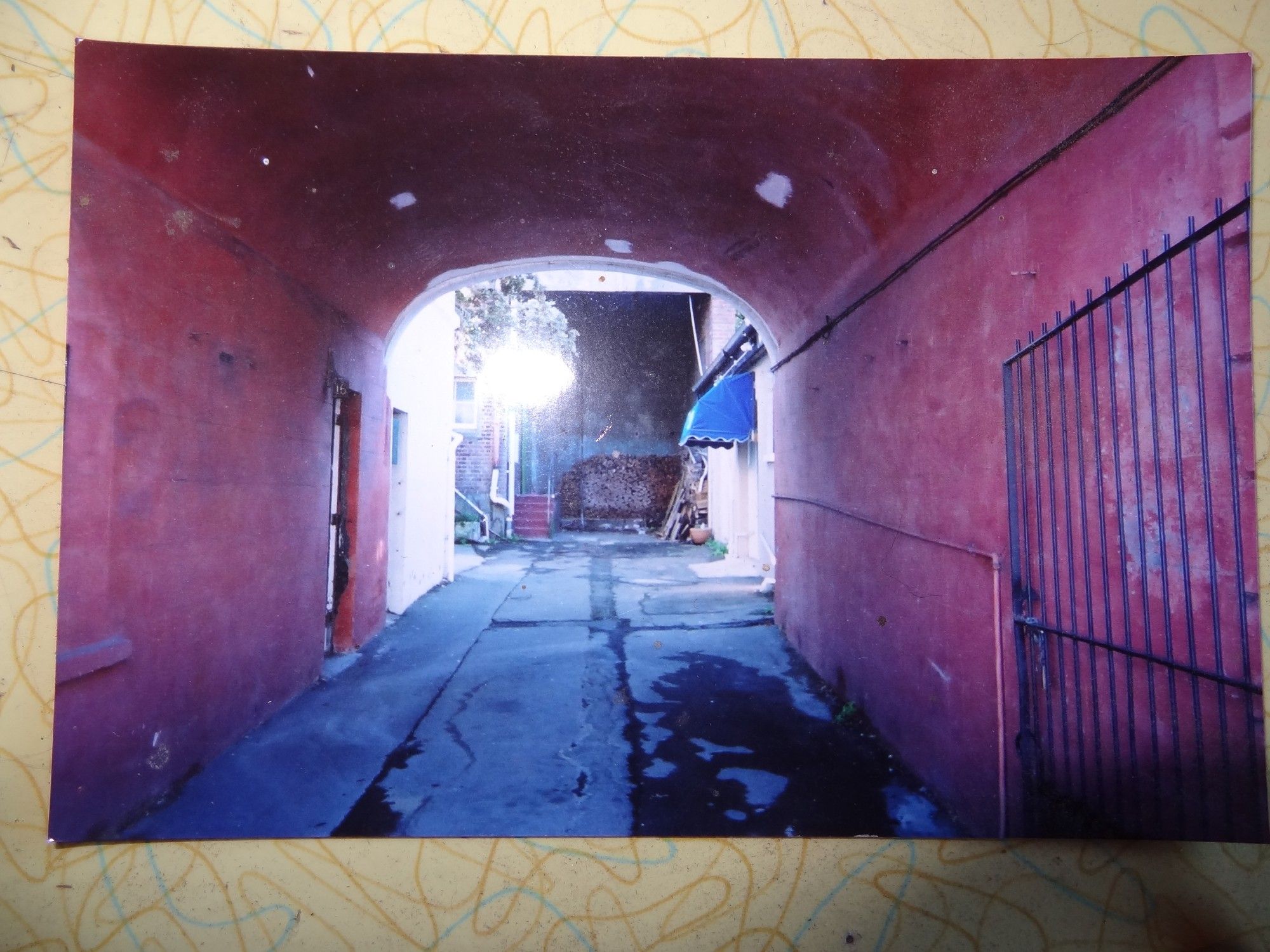 a pink archway opening into sunlight towards a wall where there is a tidy stack of firewood