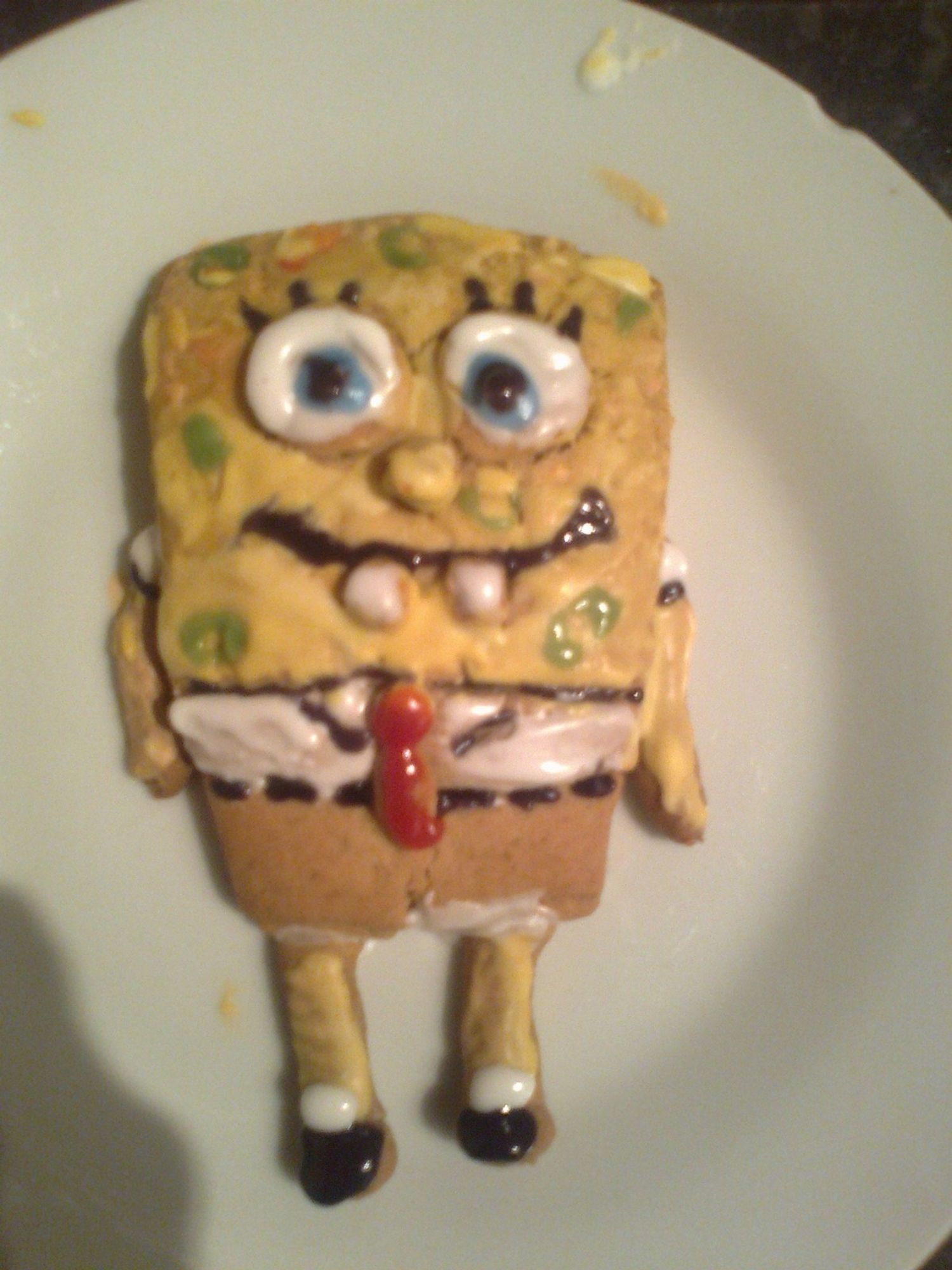 Photograph of a single SpongeBob cookie on a white plate. The plain cookie has white yellow red and brown icing to make the features of SpongeBob