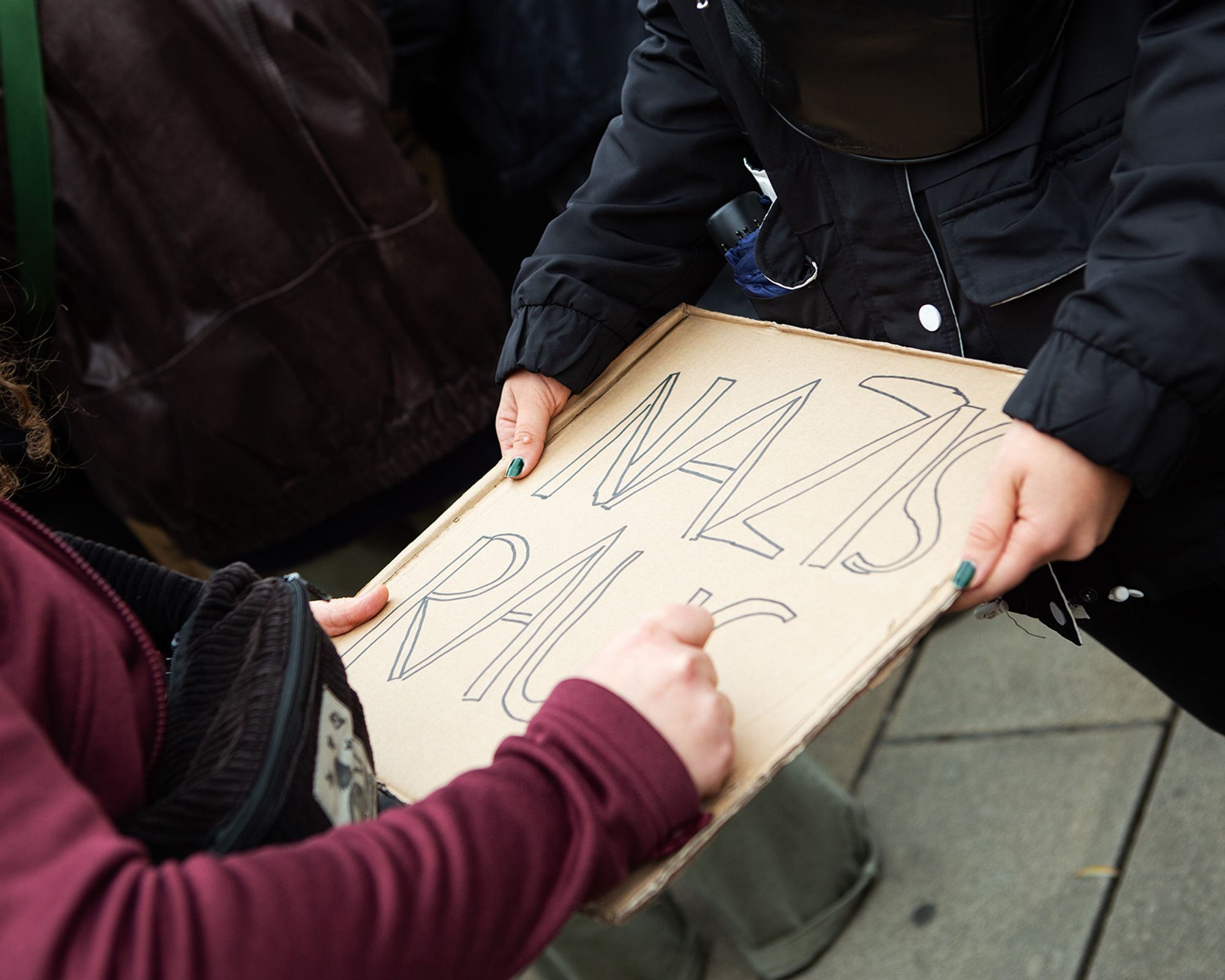 Demo gegen Rechts, zu sehen sind die Hände zweier junger Frauen, die ein Plakat malen mit der Aufschrift "Nazis raus"