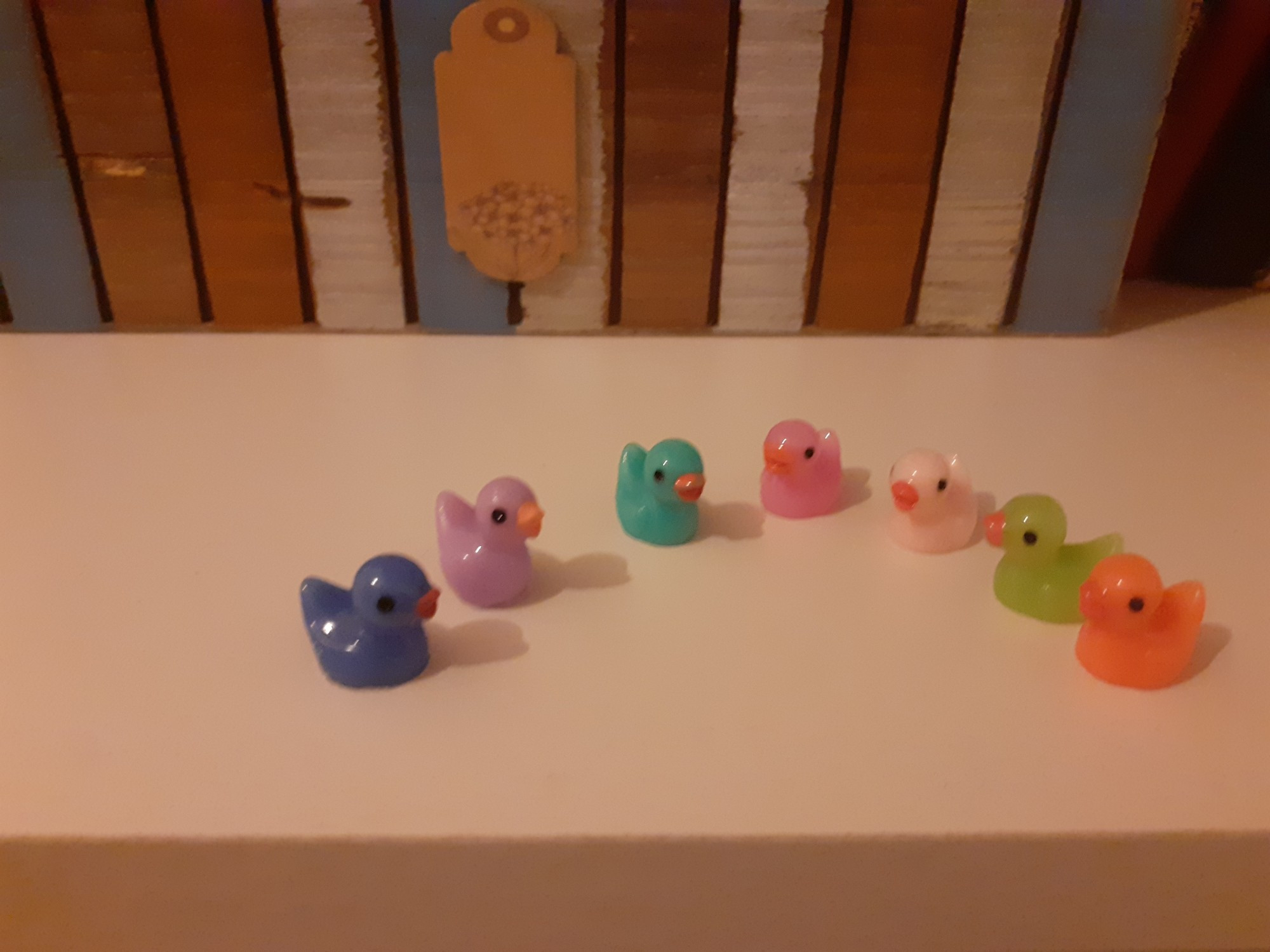 7 tiny bathtub ducks in blue  pink, mintgreen and orange on a white shelf.