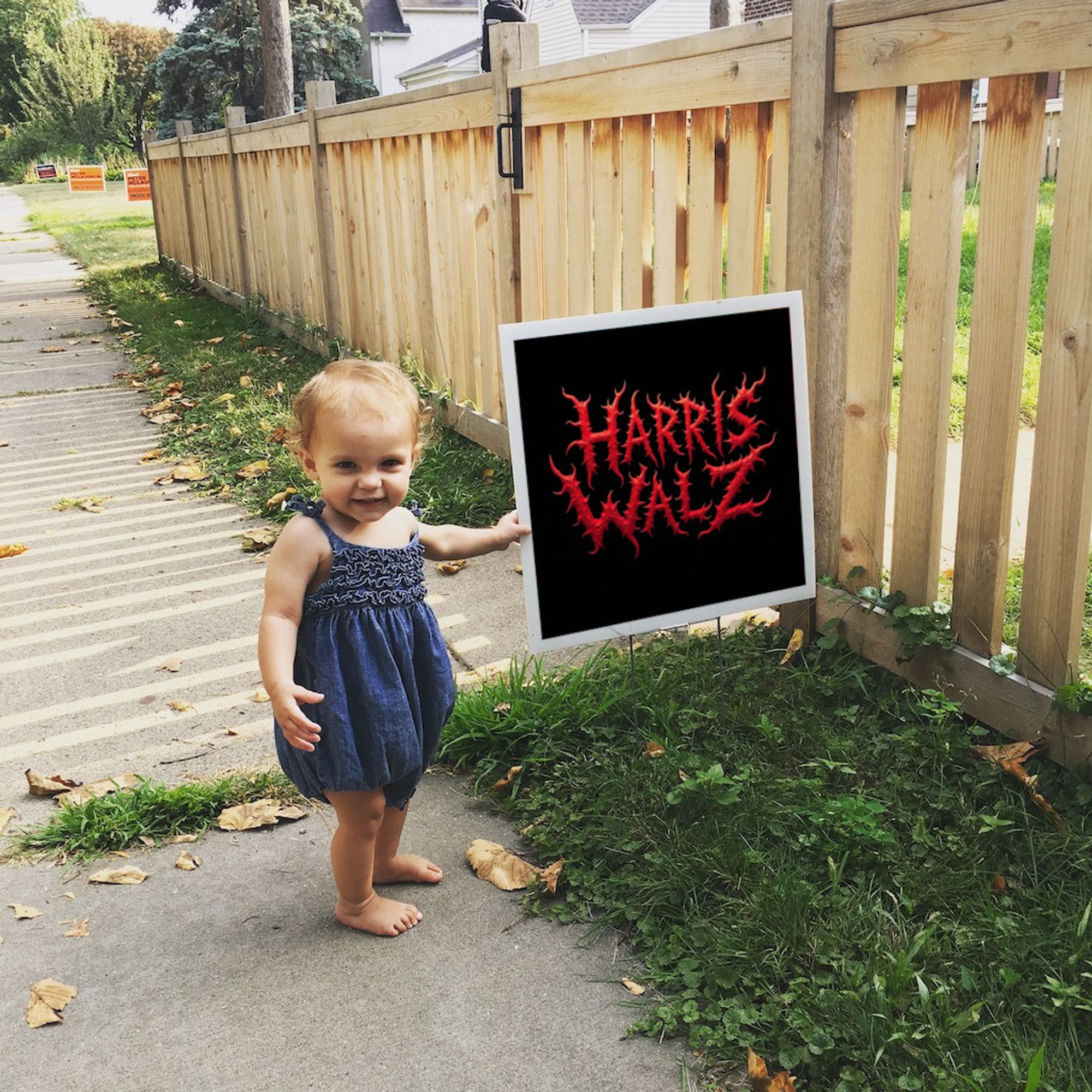 stock photo of smiling toddler in sidewalk, holding political yard sign, spikey red font on black background reading Harris Walz, looking like a death metal logo.