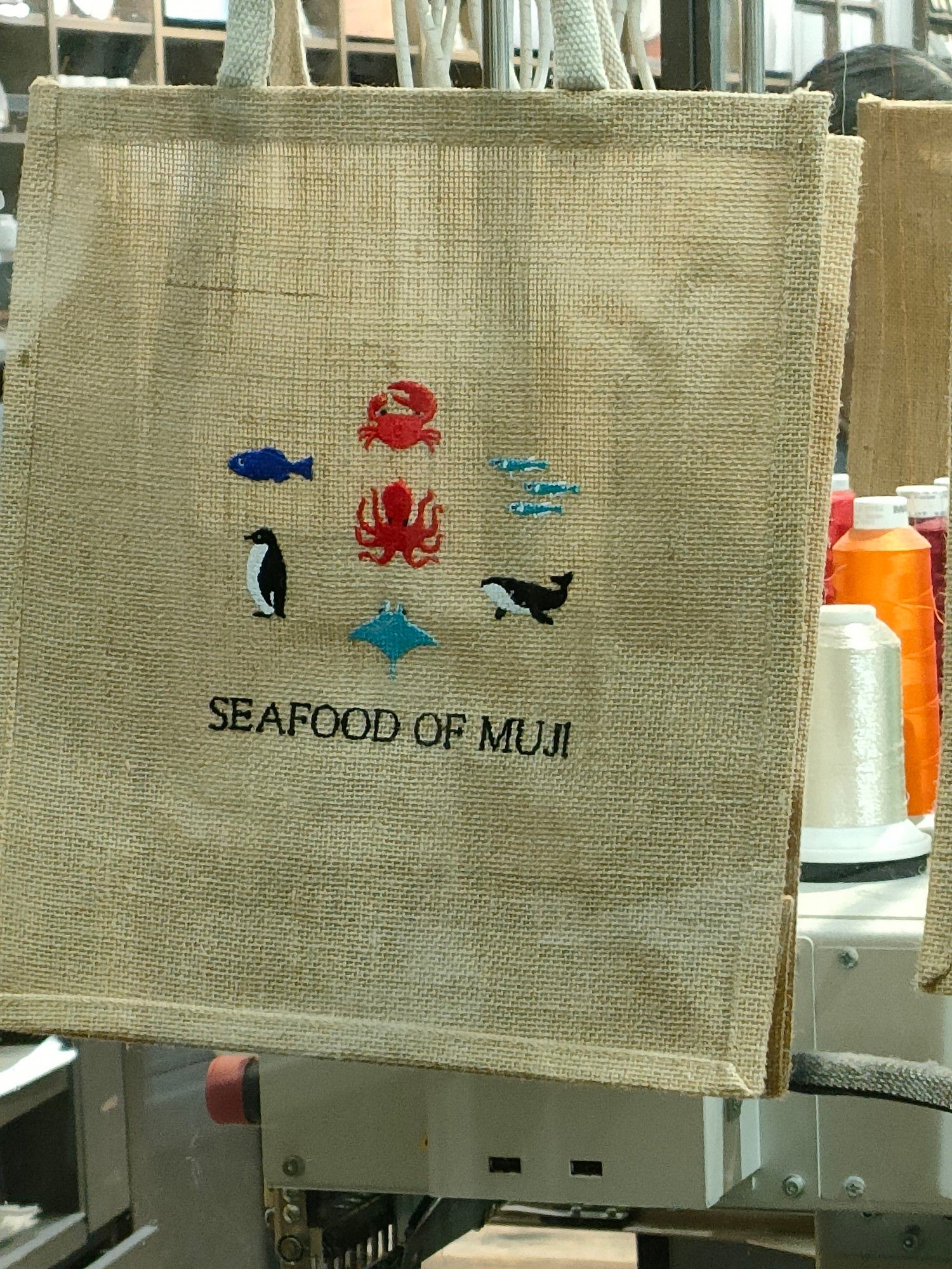 A canvas bag at the Muji shop in central Sydney showing a sample of available embroidery motifs. There's a crab, a large fish, a group of small fish, an octopus, a penguin, a whale, and a stingray. The embroidered text below the motifs says "Seafood of Muji".