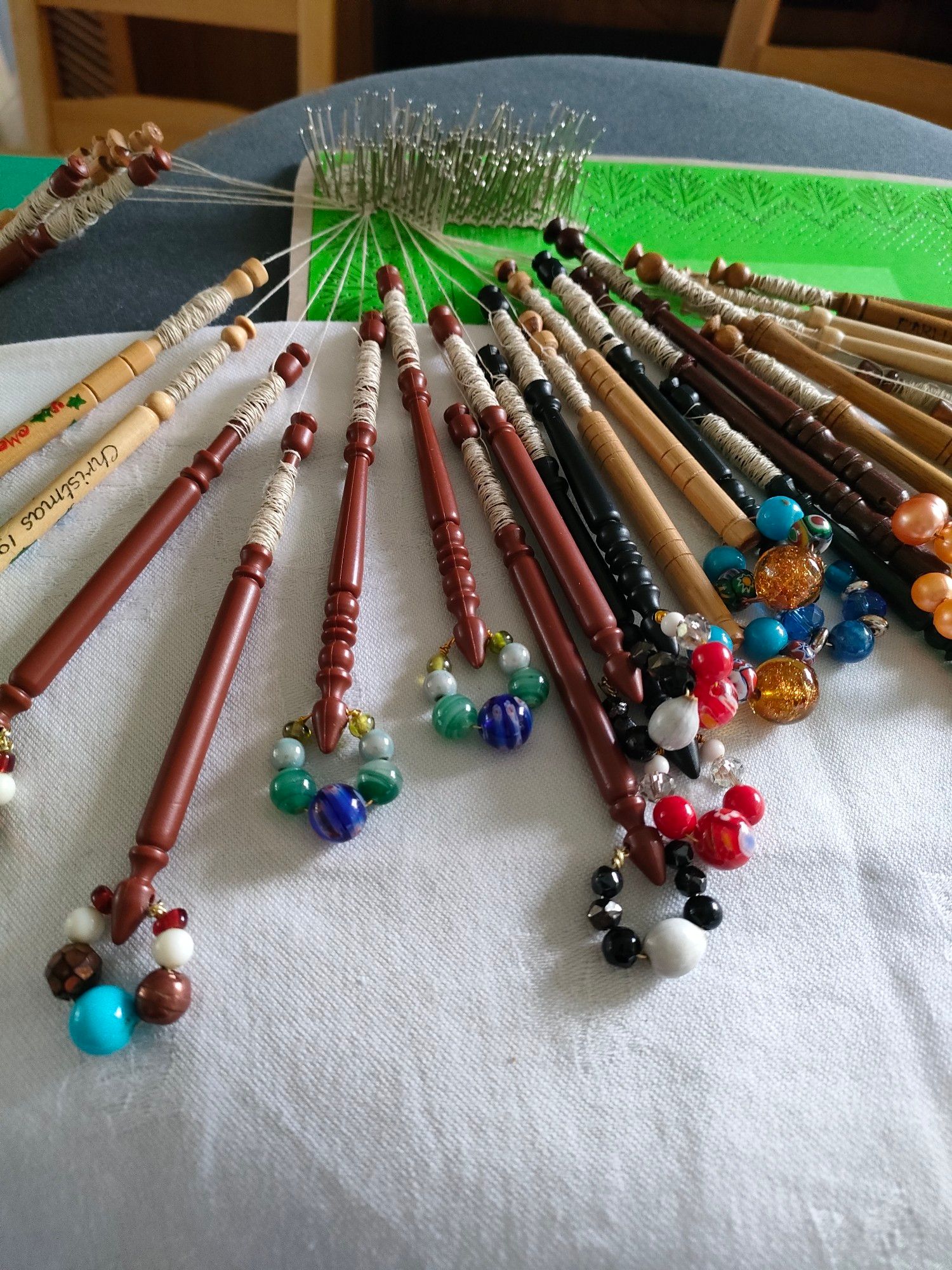 A piece of bobbin lace in progress on a cushion, with dozens of pins holding the lace in place to its pattern (the 'pricking') and 15 pairs of bobbins hanging from the working end.