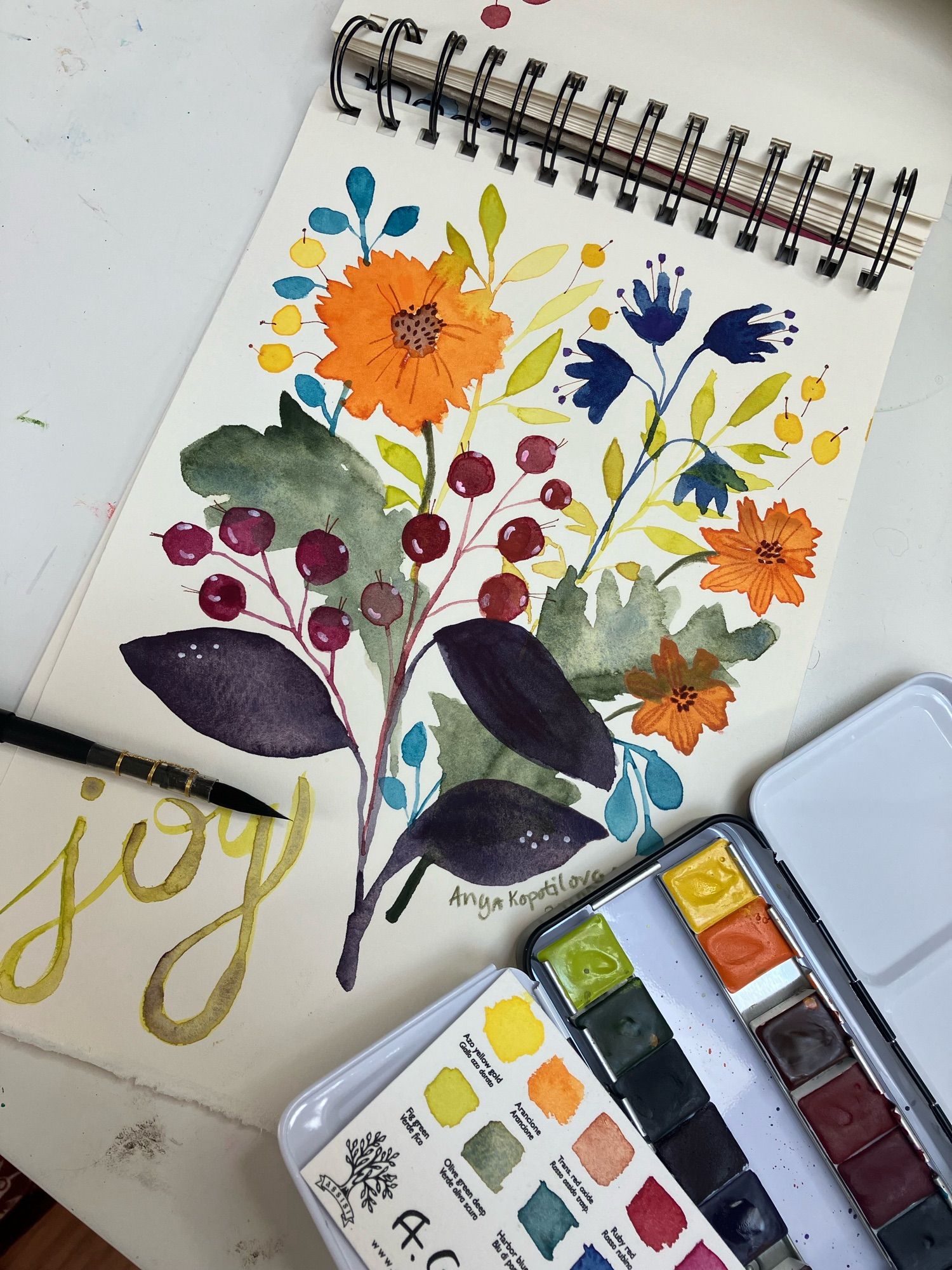 Floral sketch - orange, blue, yellow flowers, green leaves, red berries, drawing in watercolors. A brush and a box of A.Gallo watercolor pains with the swatch card.