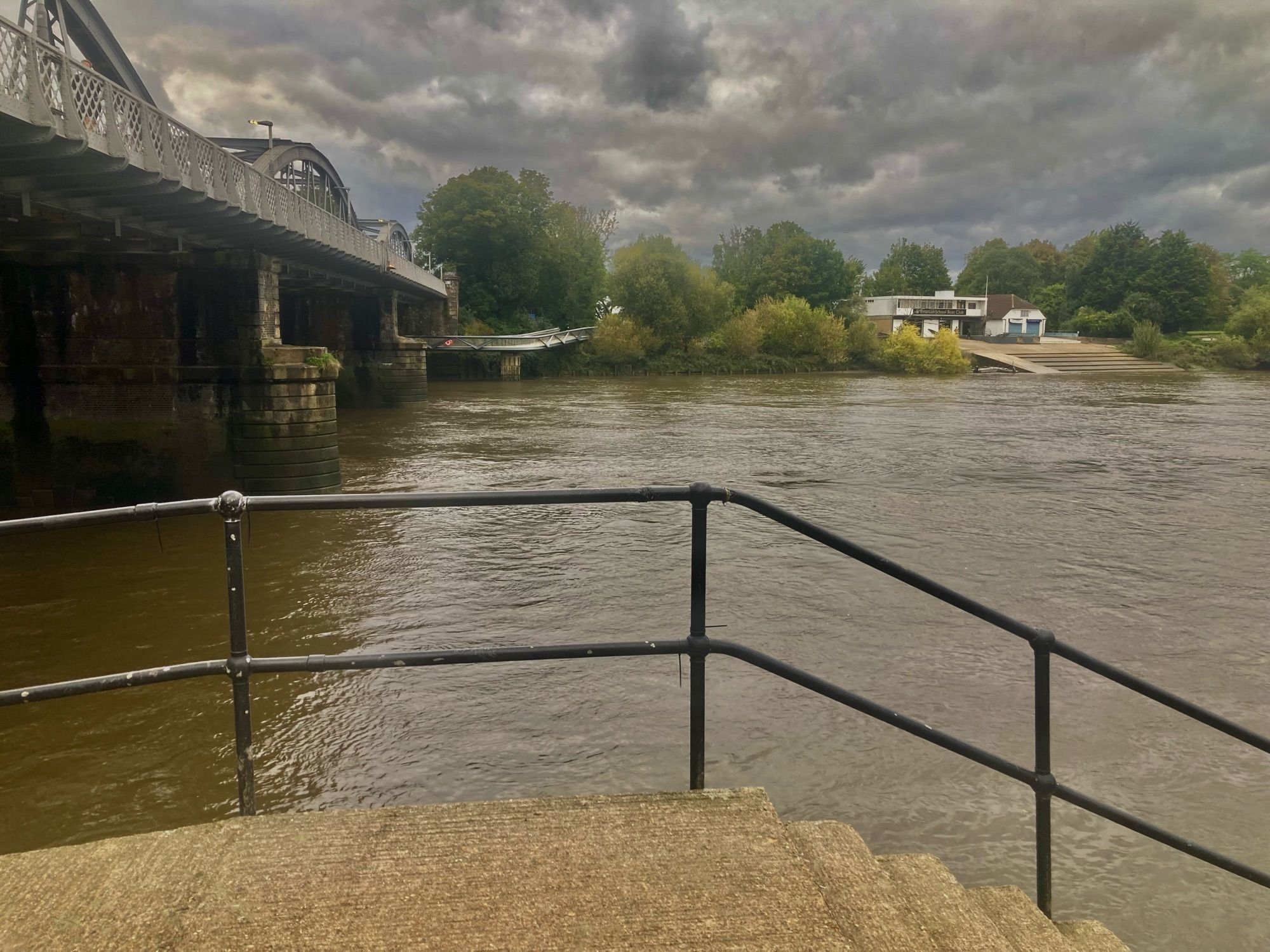 The river high and silted as it flows out from under Barnes Bridge, London, at five pm today — glowering grey skies above