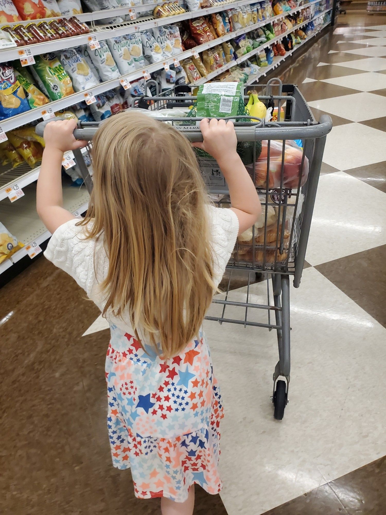 4 year old with long hair with a snarl in it pushing a grocery cart in the store