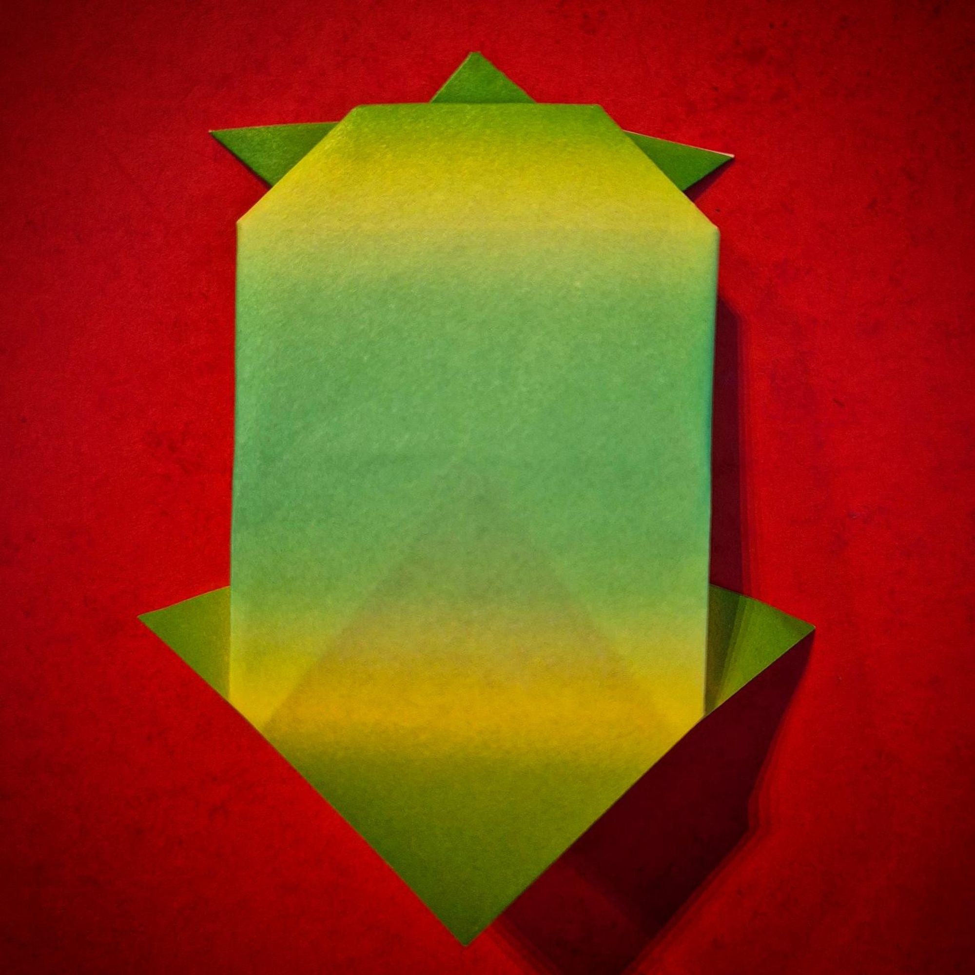 Photo of an origami turtle folded out of paper in different shades of green, on top of a bright red background.