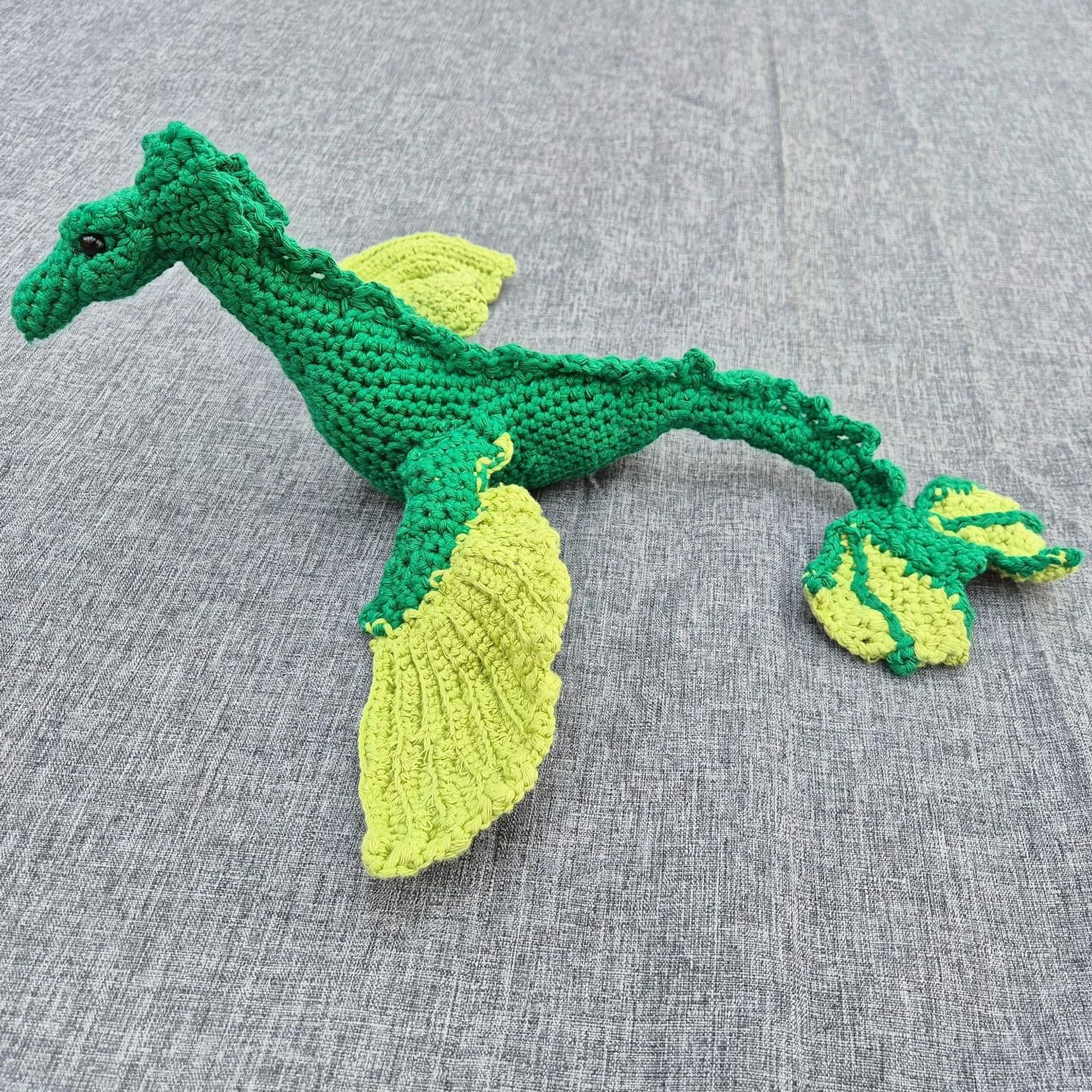 Photo of a crocheted sea dragon with a dark green body and light green details on its wings and tail.