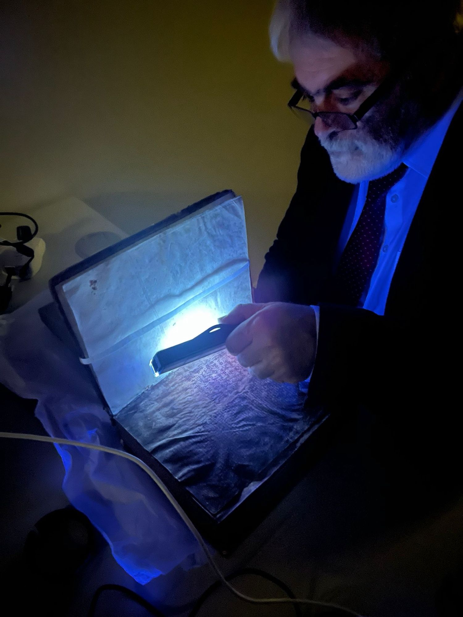 Man shining an ultraviolet light on a manuscript