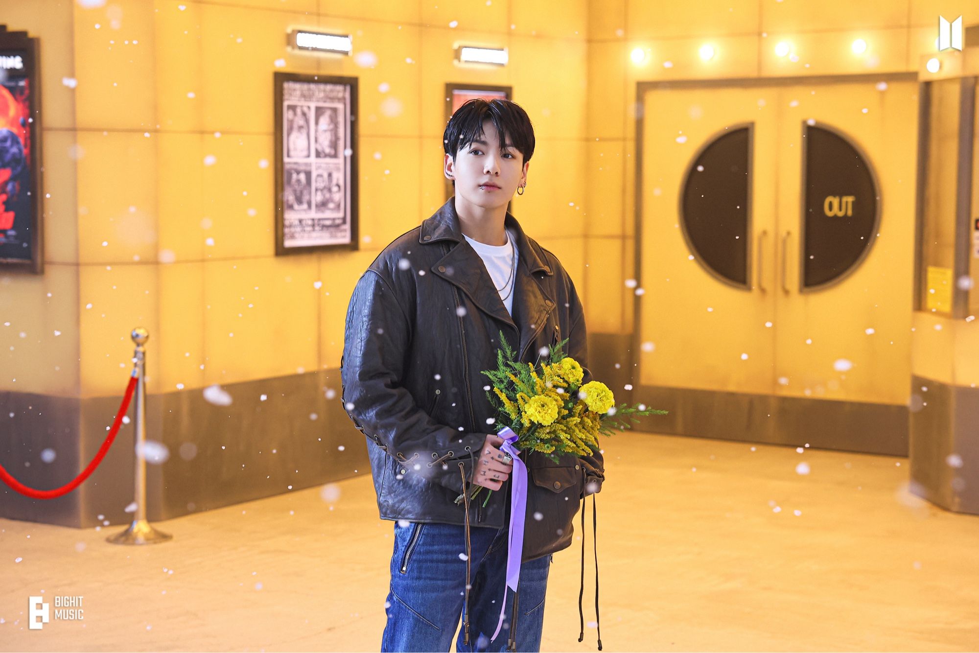 Jungkoon standing outside of a theater holding a bouquet with purple ribbon