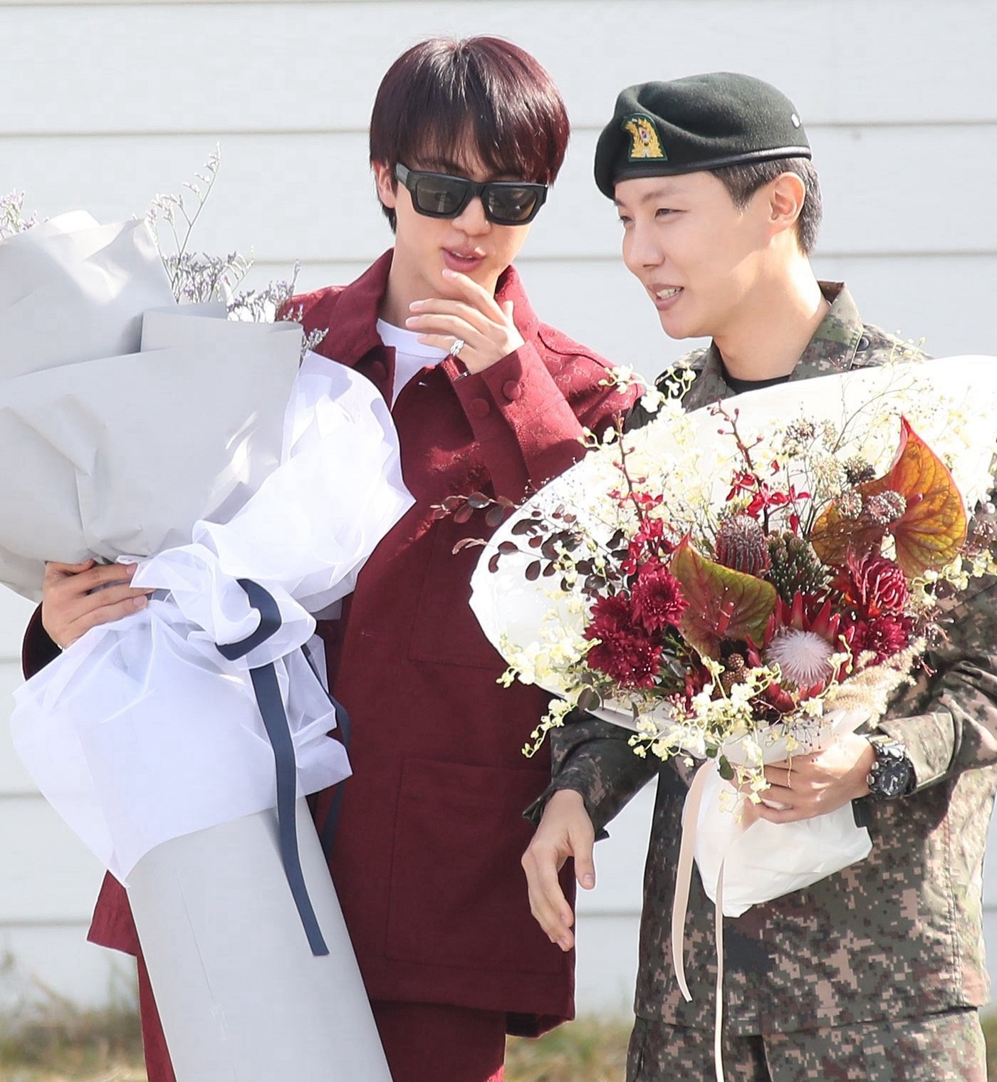 Seokjin in his burgundy Gucci suit and sunglasses, holding a massive boquet and talking to Hobi— Hobi in his full military uniform and beret, also holding a bouquet of flowers. 