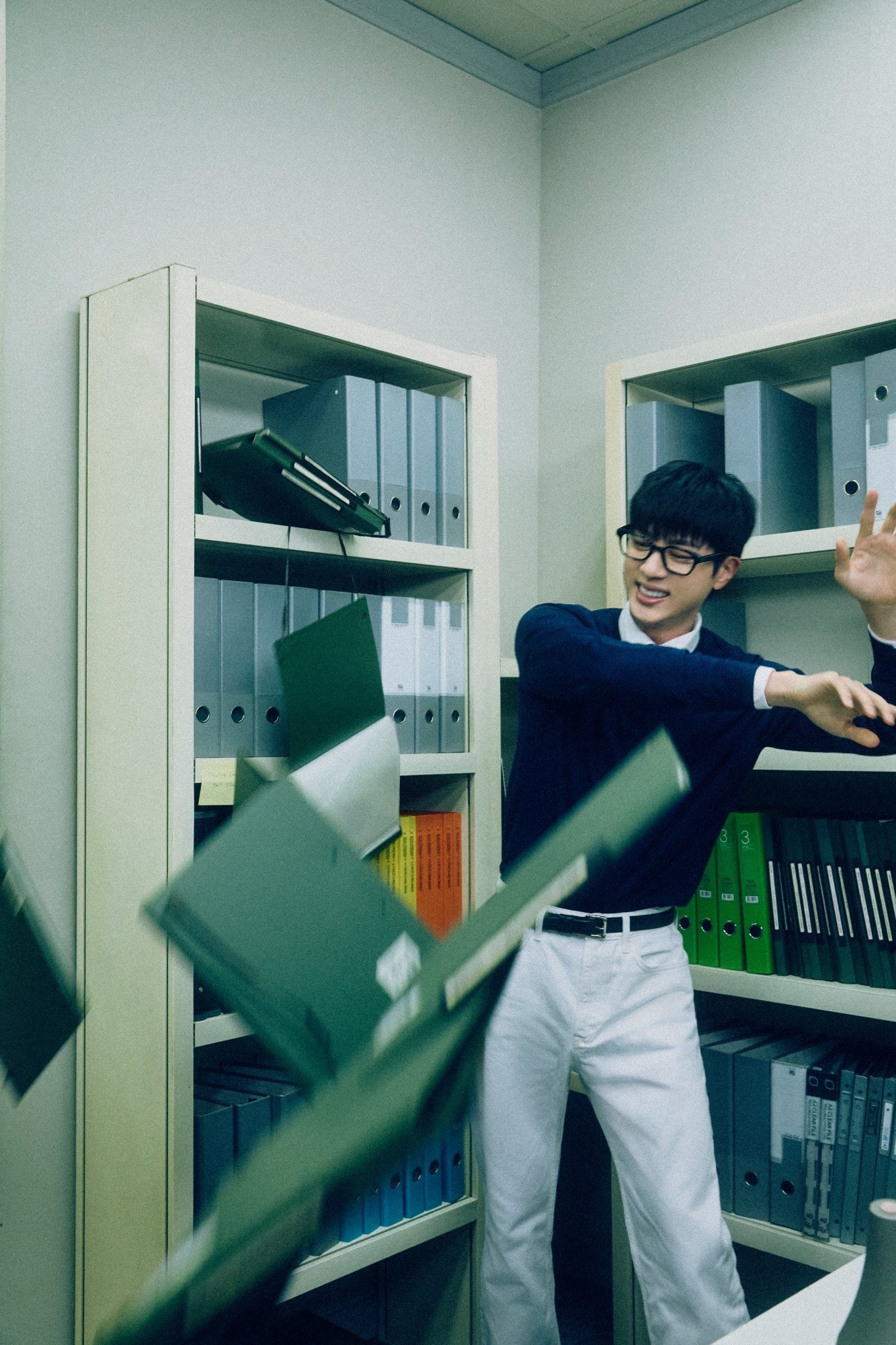 Seokjin in a smart casual attire with glasses mid-throw of documents, beaming beightly