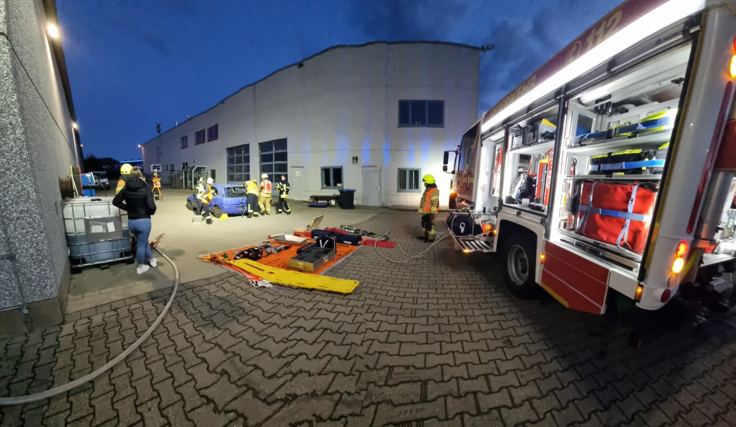 Gestriges Feuerwehrüben. Autozerlegung.
Man sieht wie die Feuerwehr ein blaues Auto zerlegt zwecks Menschenrettung. Ziel: große Seitenöffnung. Davor ist ein Materiallagerplatz auf einer roten Plane zu sehen. Davor steht ein HLF 20  und ein Maschinist.