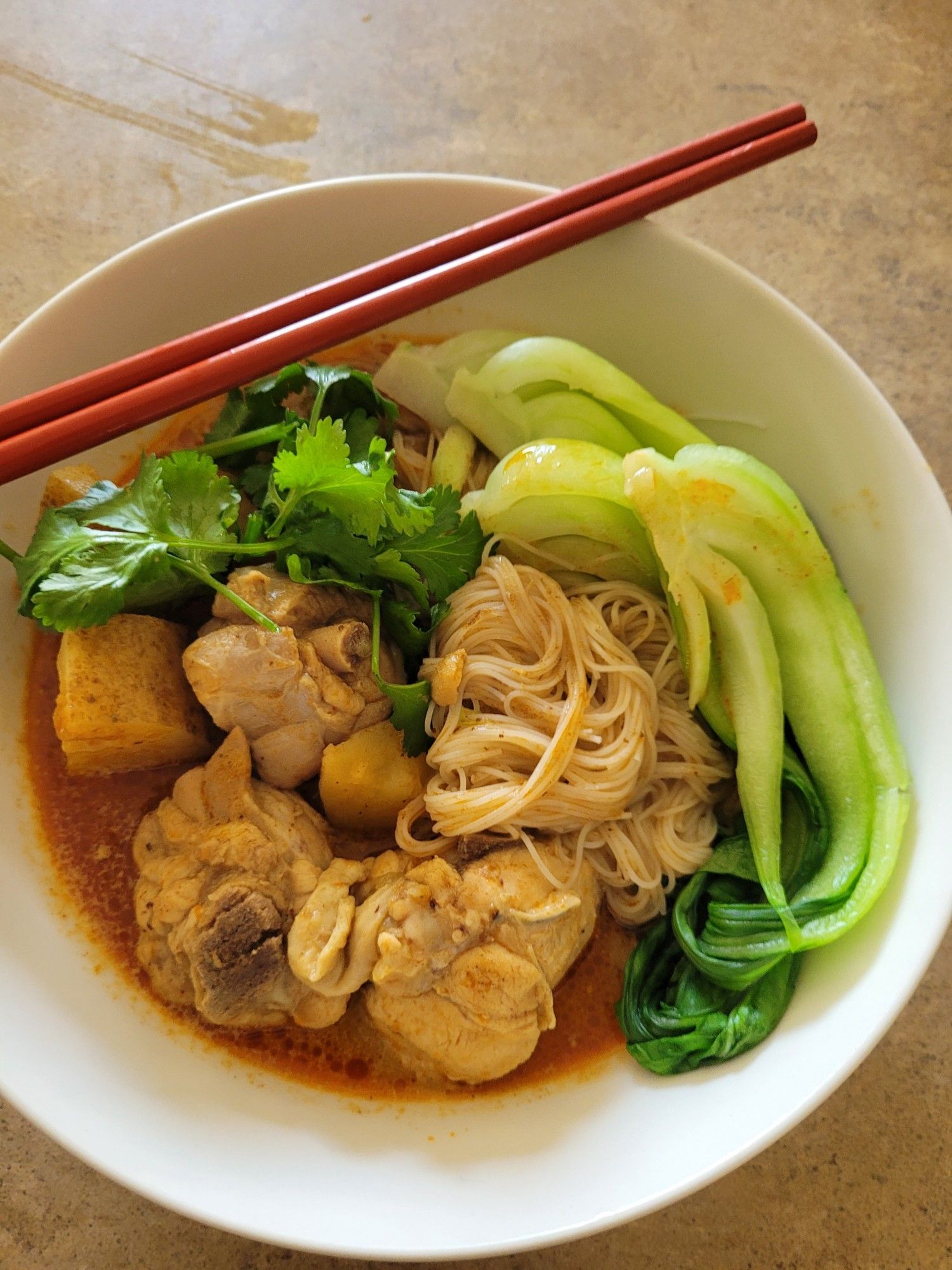 Dinner as described served up in a white bowl, with a pair of red chopsticks laying atop the bowl on a diagonal