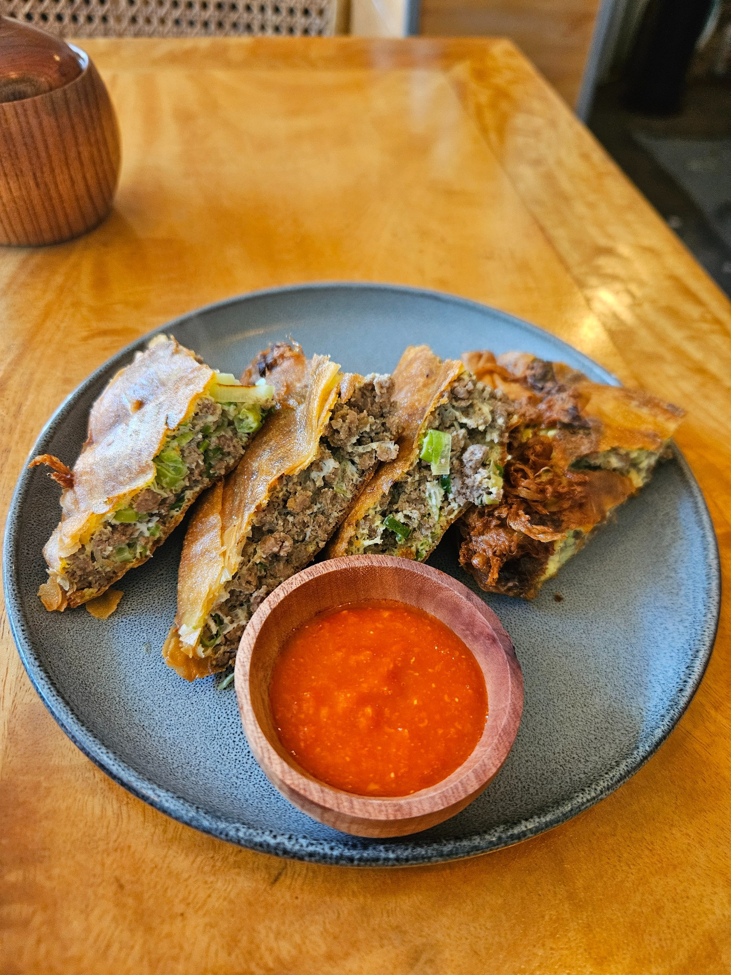 The martabak, already cut into quarters arranged on a plate, with a small bowl of chilli sauce to accompany.