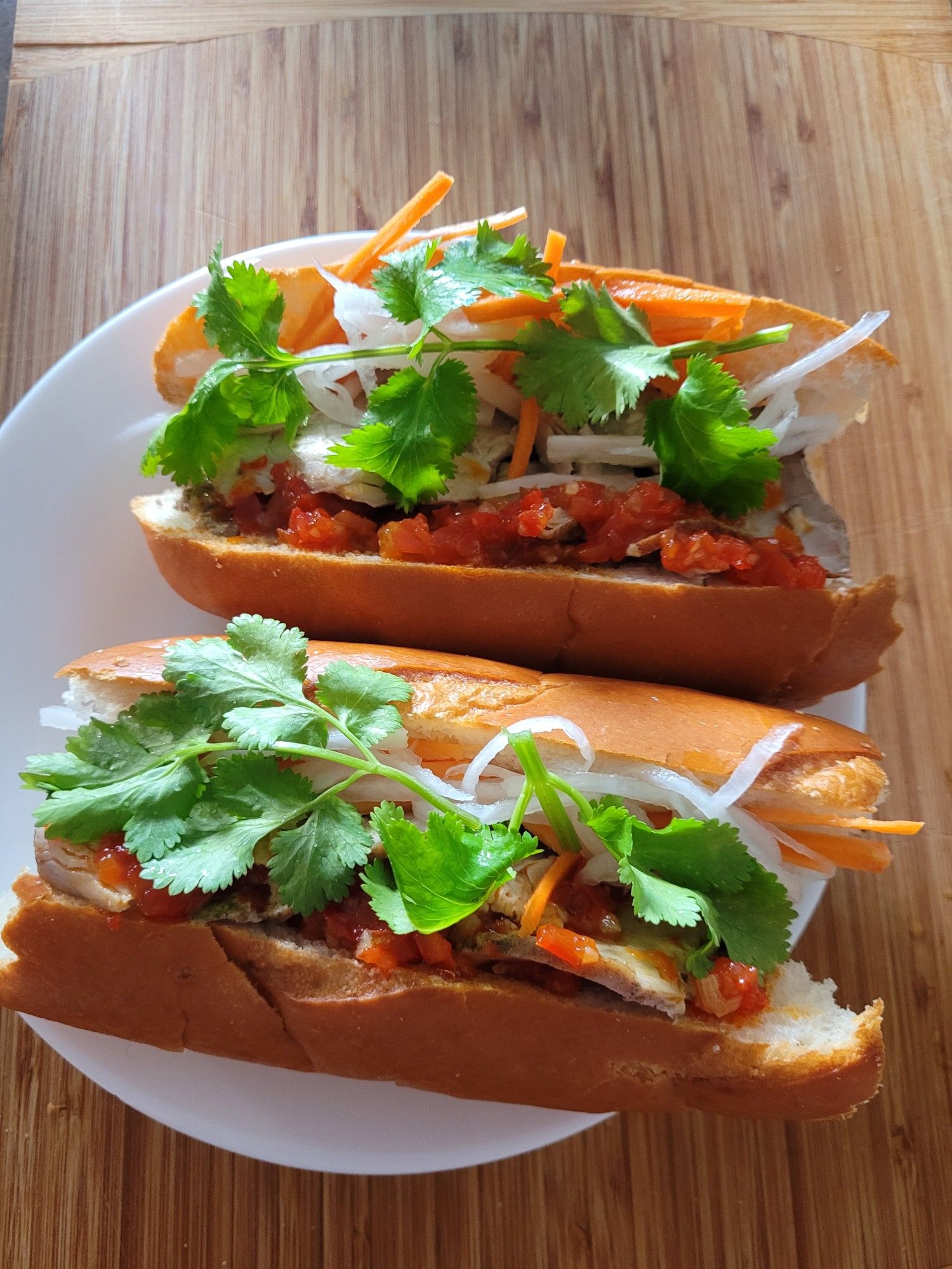 Two banh mi sandwich rolls on a round white soup plate.