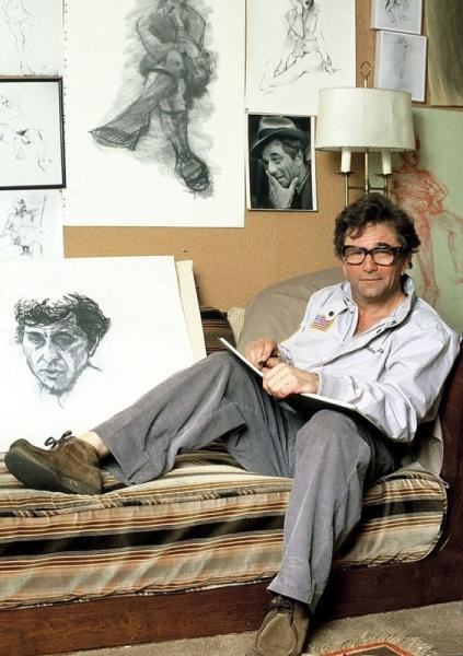 Peter Falk with big glasses drawing a picture while sitting on a couch, he was a prolific artist and drew all the time because he really was perfect. Physically unable to button the last 3 buttons of his shirt