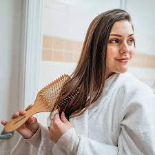 a product photo of a woman brushing her hair with a large wooden paddle-shaped brush