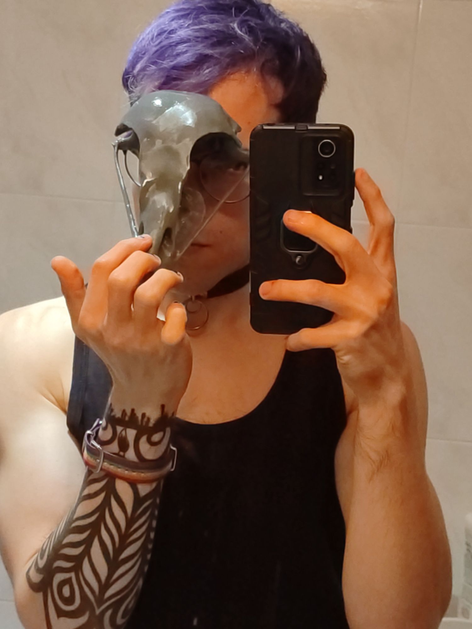 mirror selfie of a violet haired person, with a tattooed left arm(right due to mirror) holding a 3d printed bird skull in front of their face