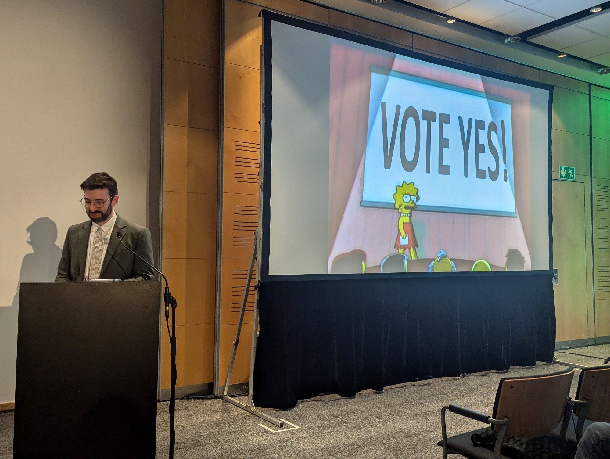 Peter Tennant stood in front of a shameless slide that says 'Vote Yes'.