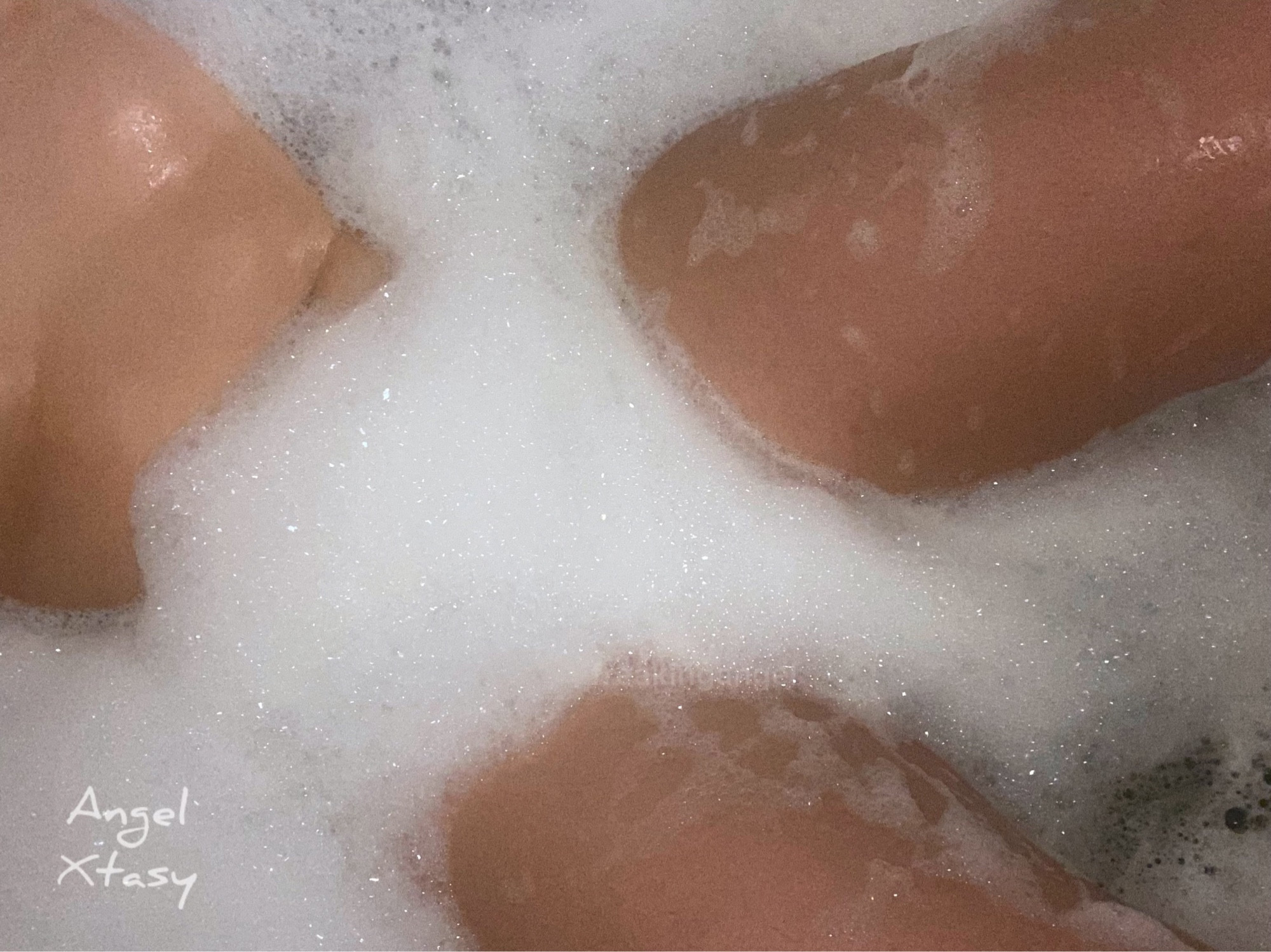 Angel Xtasy, asian transmasc, in a bubble bath. They are pictured from below the chest to above their knees, bubbles completely cover in between their legs and lower torso, as well as surrounds the rest of their body