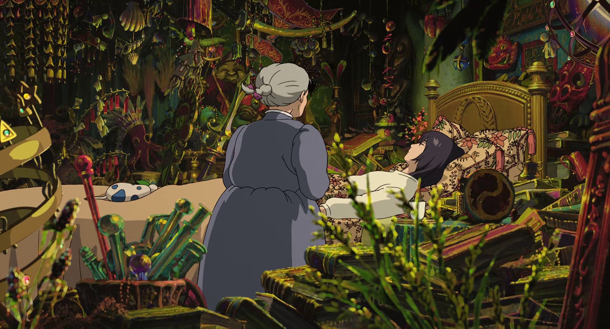 Screenshot from Howl's Moving Castle showing Howl's room absolutely stuffed to the gills with strange trinkets, jewelry and artifacts. This shot is a bit further away showing more of the room, and Sophie standing in front of Howl sleeping on his bed amid the mess